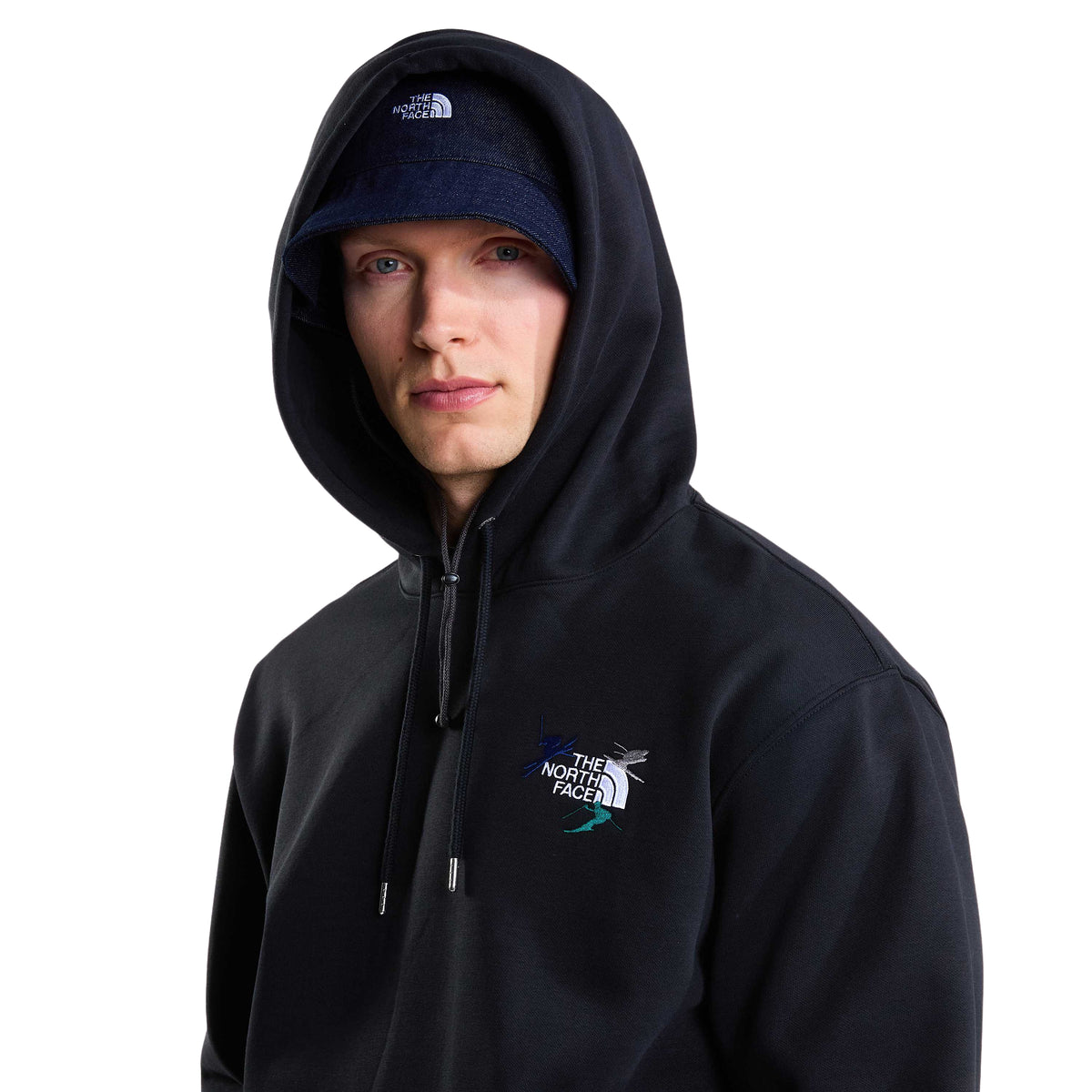 Vista aproximada da sweat The North Face Off Piste Embro preta num modelo, com capuz colocado sobre o chapéu e bordado no peito.
