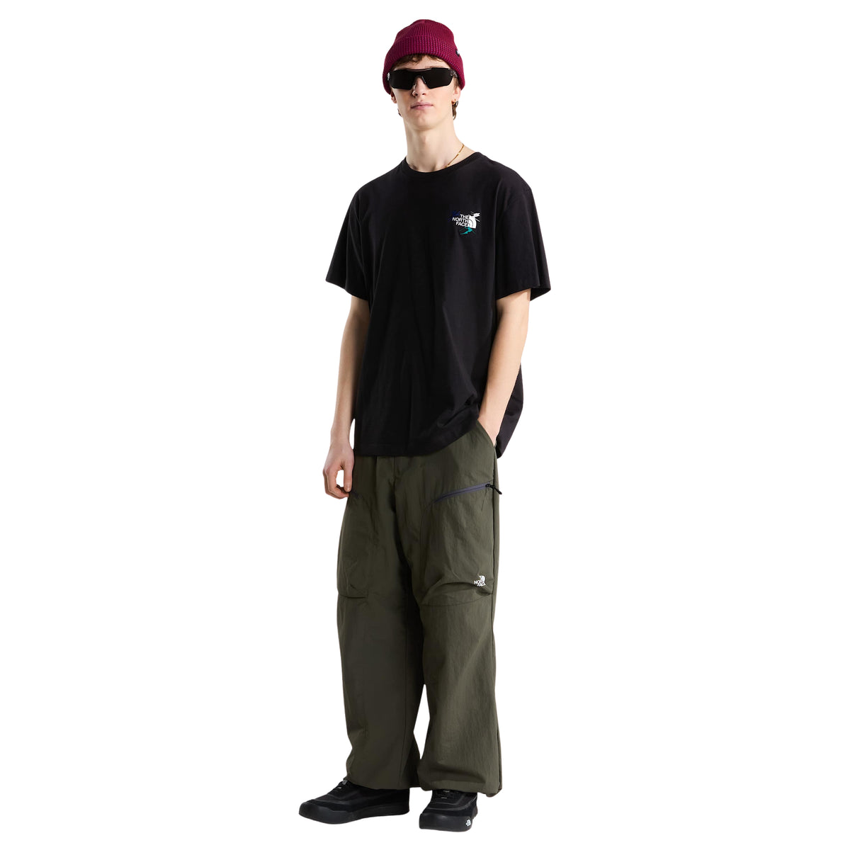Modelo de corpo inteiro com t-shirt The North Face Off Piste Embro preta, calças verde-escuras e gorro bordeaux.