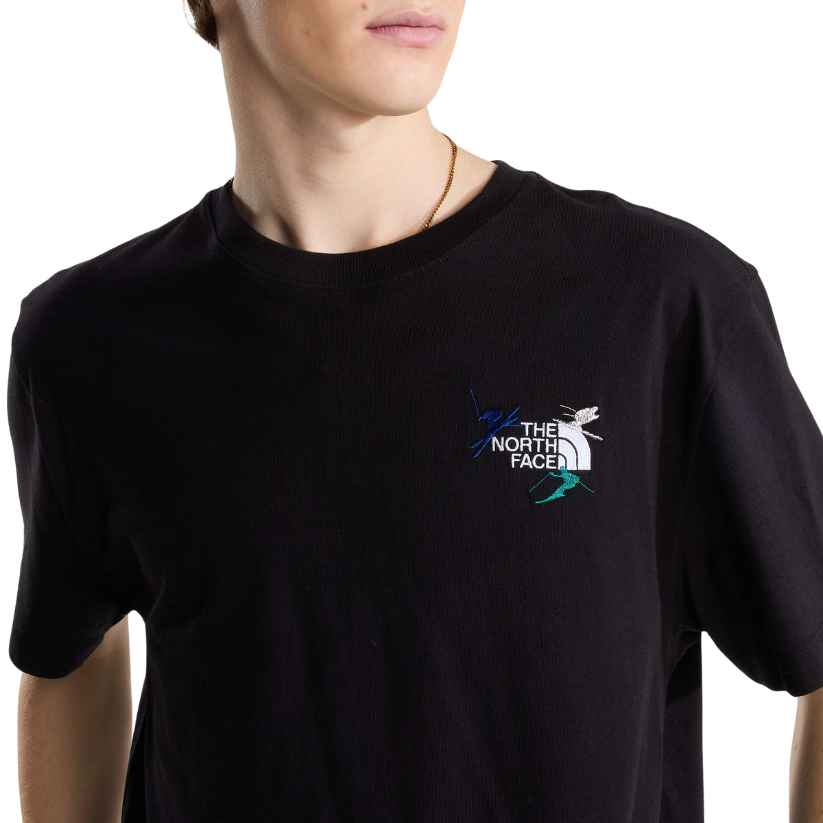 Pormenor do bordado no peito da t-shirt The North Face Off Piste Embro preta, com logótipo branco e figuras de esquiadores.