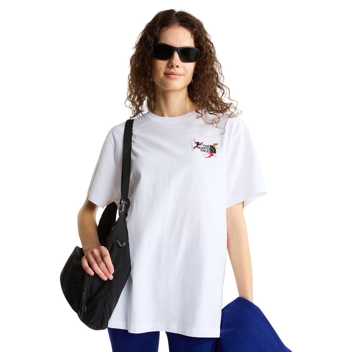 Modelo com t-shirt The North Face Off Piste Embro branca, óculos de sol e bolsa preta ao ombro, com bordado no peito visível.