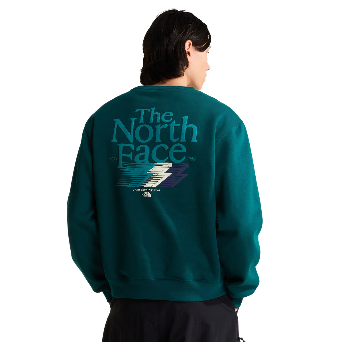 Sweatshirt para homem The North Face Retro Trail Relaxed Crew em Pacific Teal — modelo masculino de costas, meio corpo, malha polar teal, gráfico Retro Trail em relevo de camurça nas costas com "The North Face" em tipografia vintage e raio colorido, "Trail Running Club" por baixo, gola canelada, corte relaxed, calças pretas, fundo branco.