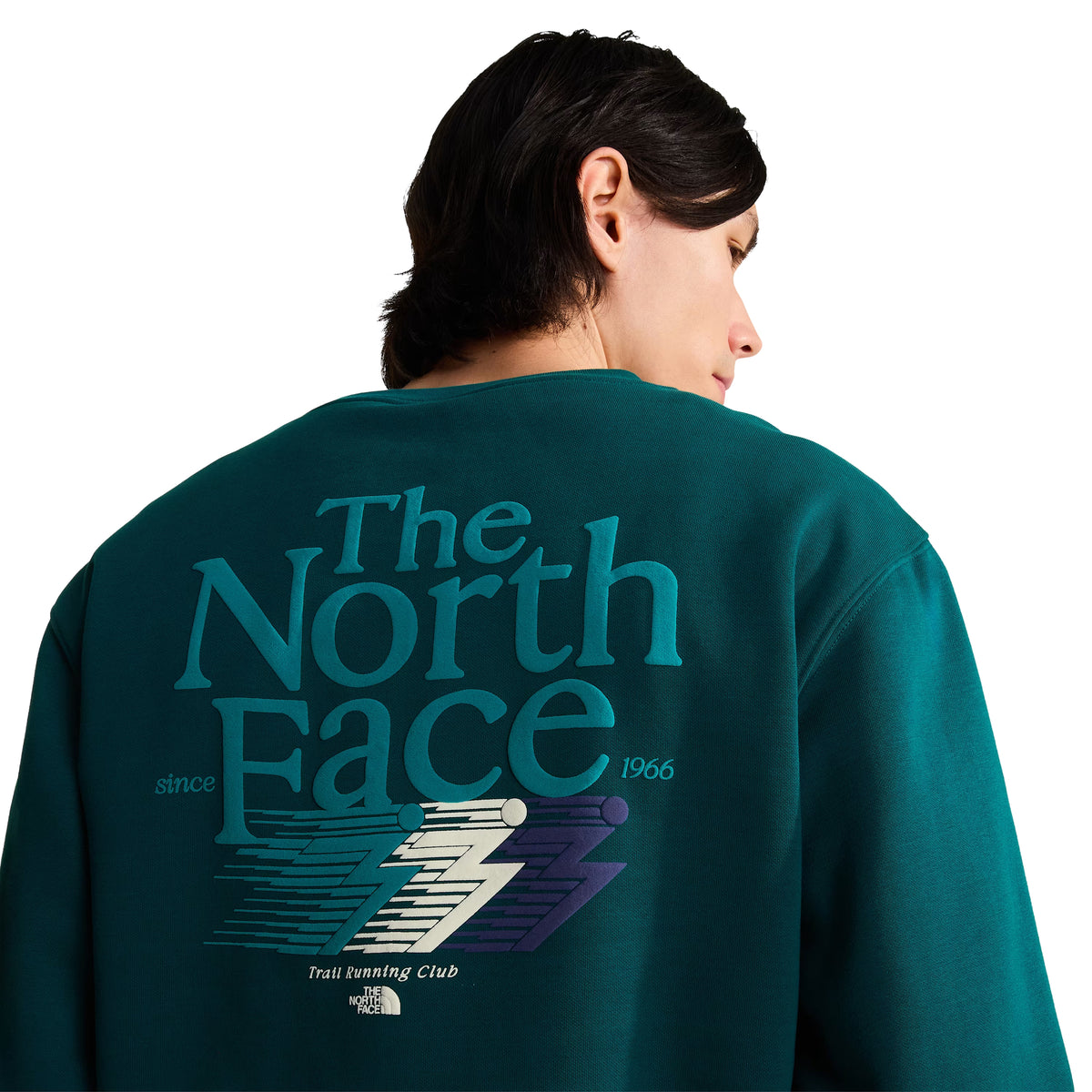 Sweatshirt para homem The North Face Retro Trail Relaxed Crew em Pacific Teal — detalhe das costas em close-up, modelo feminino, malha polar teal, gráfico Retro Trail em relevo de camurça com "The North Face since 1966" em tipografia vintage, raio creme e azul escuro, "Trail Running Club" por baixo, fundo branco.