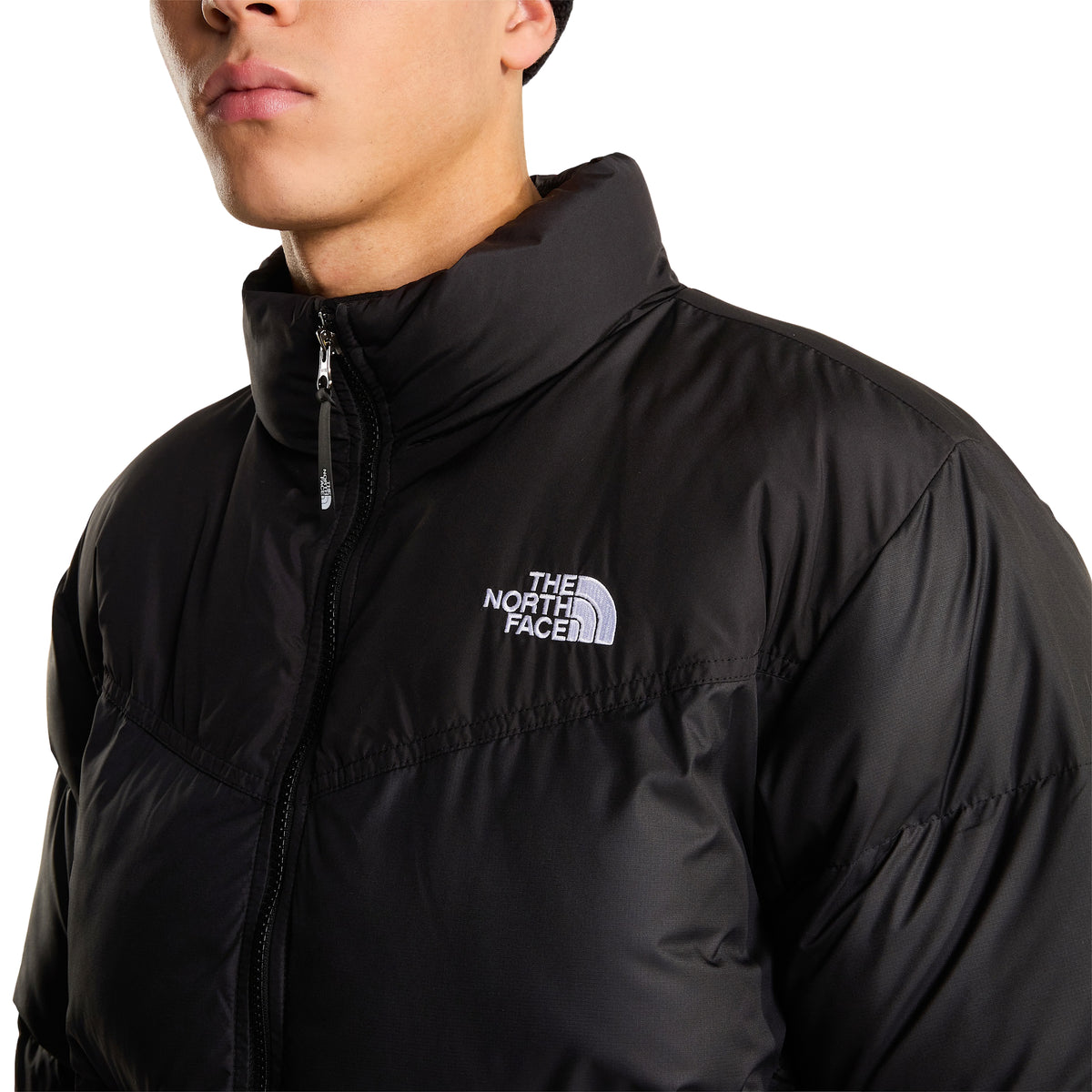 Pormenor do logótipo branco The North Face bordado no peito do casaco Saikuru preto, com gola levantada e fecho central.