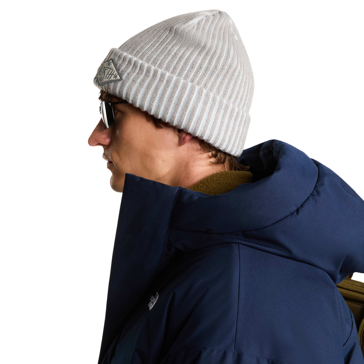 Vista lateral do gorro The North Face Salty Lined SE Stone Slab num modelo com óculos de sol e casaco azul-escuro.