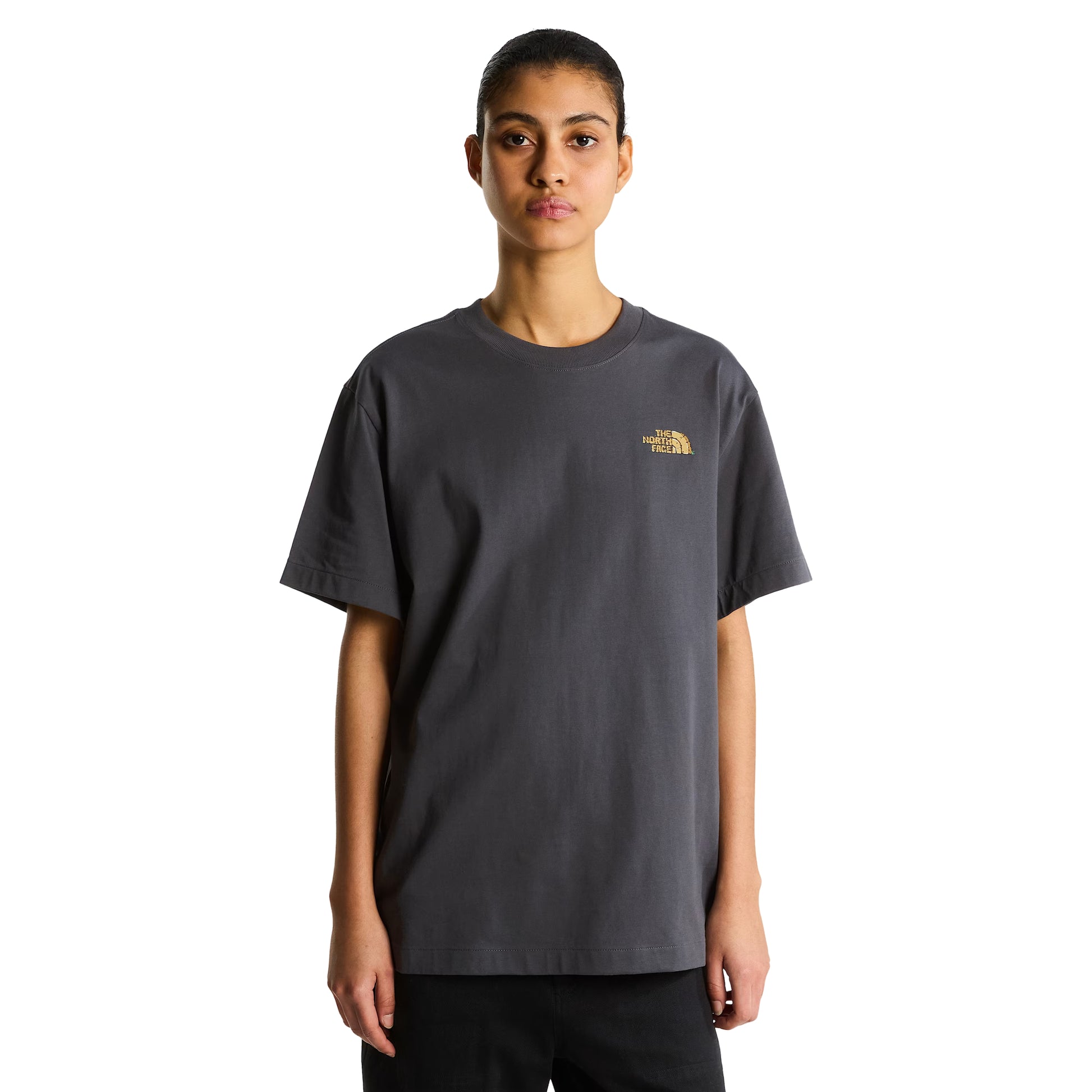 T-Shirt The North Face Stone Logo Relaxed em Anthracite Grey — modelo feminino de frente, cabelo apanhado, calças pretas, logo TNF em dourado no peito esquerdo visível, corte relaxed oversized, fundo branco.