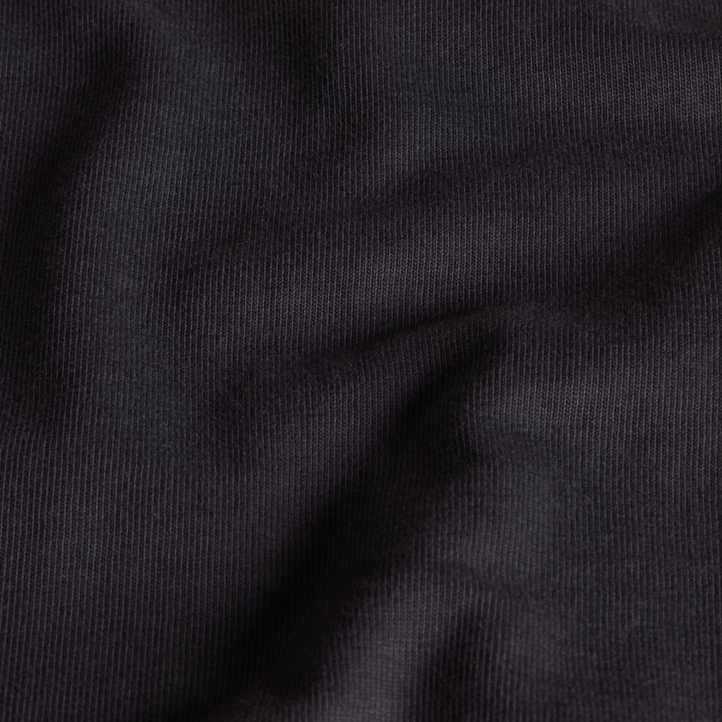 T-Shirt The North Face Stone Logo Relaxed em Anthracite Grey — detalhe do peito de modelo feminino, logo The North Face Stone em dourado/ocre no peito esquerdo e gola redonda em Anthracite Grey visíveis em close-up, fundo branco.