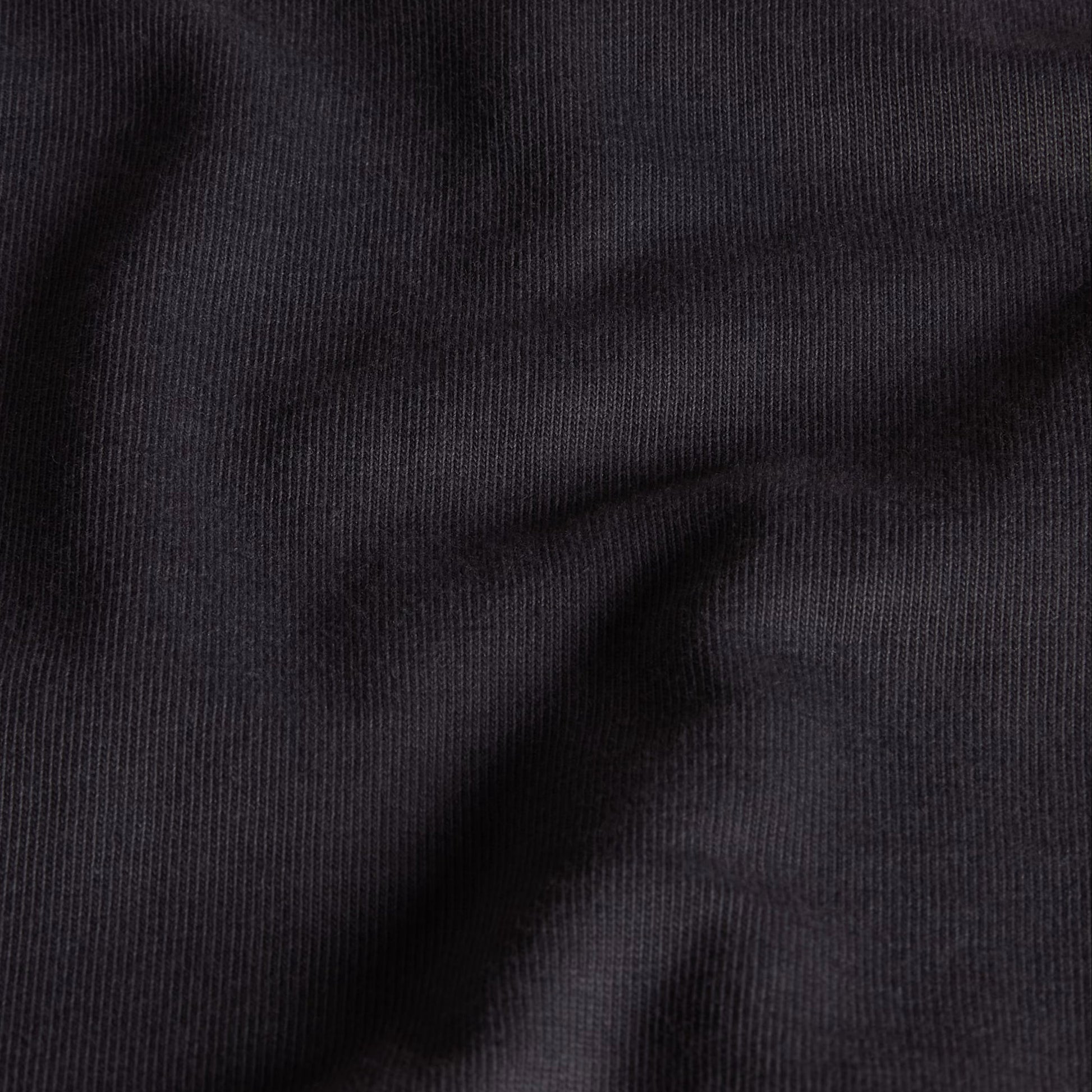 T-Shirt The North Face Stone Logo Relaxed em Anthracite Grey — detalhe do peito de modelo feminino, logo The North Face Stone em dourado/ocre no peito esquerdo e gola redonda em Anthracite Grey visíveis em close-up, fundo branco.