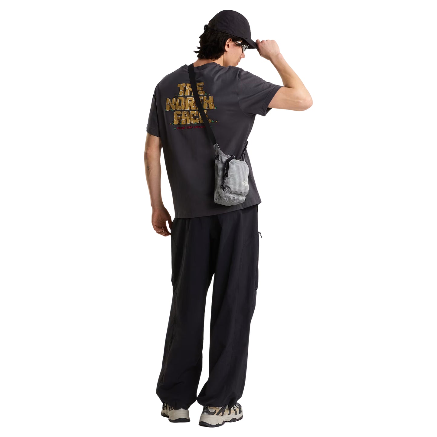 T-Shirt The North Face Stone Logo Relaxed em Anthracite Grey — detalhe das costas com modelo masculino, gráfico "The North Face" estilo pedra em dourado/ocre com detalhes verdes e inscrição "Never Stop Exploring" em vermelho na base, fundo branco.