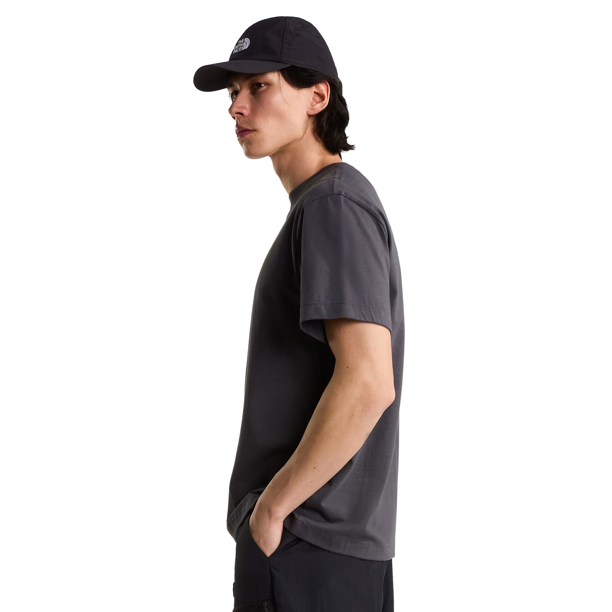 T-Shirt The North Face Stone Logo Relaxed em Anthracite Grey — modelo masculino de perfil esquerdo, boné TNF preto, calças pretas, silhueta do corte relaxed visível, fundo branco.