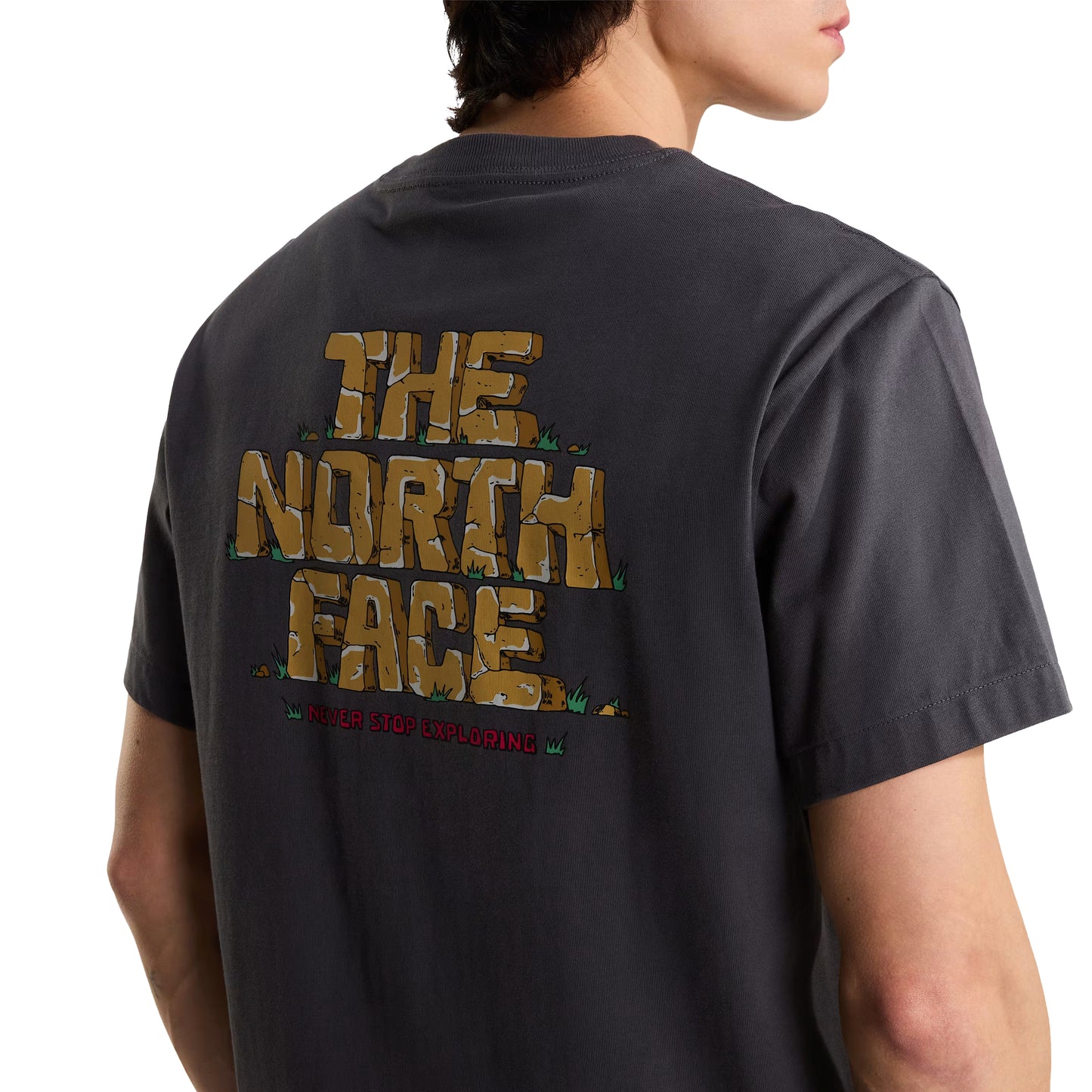 T-Shirt The North Face Stone Logo Relaxed em Anthracite Grey — modelo feminino de costas a 3/4, corpo inteiro, calças pretas largas e sapatilhas bege TNF, tote bag TNF em cru na mão direita, gráfico Stone Logo nas costas parcialmente visível, fundo branco.