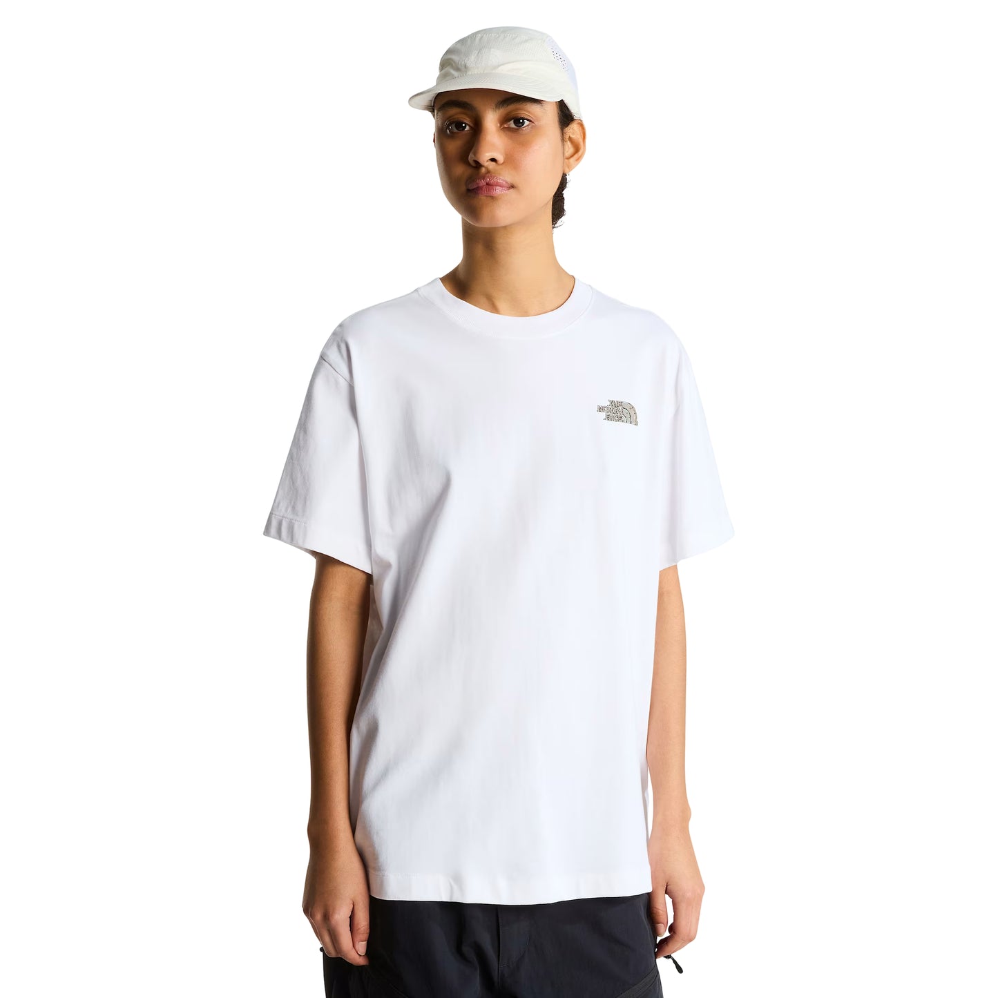 T-Shirt The North Face Stone Logo Relaxed em TNF White — modelo feminino de frente, boné TNF branco perfurado, calças pretas cargo, logo TNF Stone em verde musgo/caqui no peito esquerdo e gola redonda visíveis, corte relaxed oversized, fundo branco.