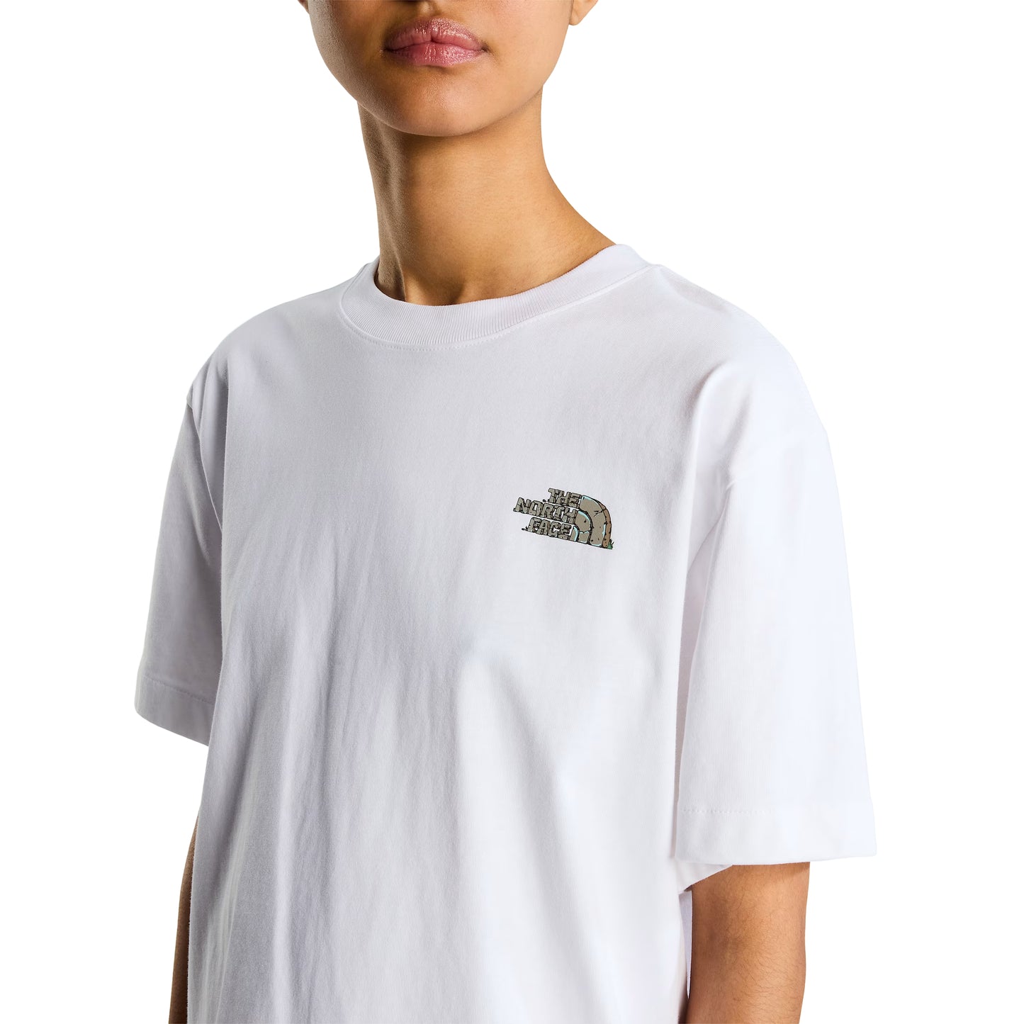 T-Shirt The North Face Stone Logo Relaxed em TNF White — detalhe do peito de modelo feminino, logo TNF Stone Logo em pedra cinza/verde musgo com half-dome no peito esquerdo e gola redonda em TNF White visíveis em close-up, corte relaxed oversized, fundo branco.