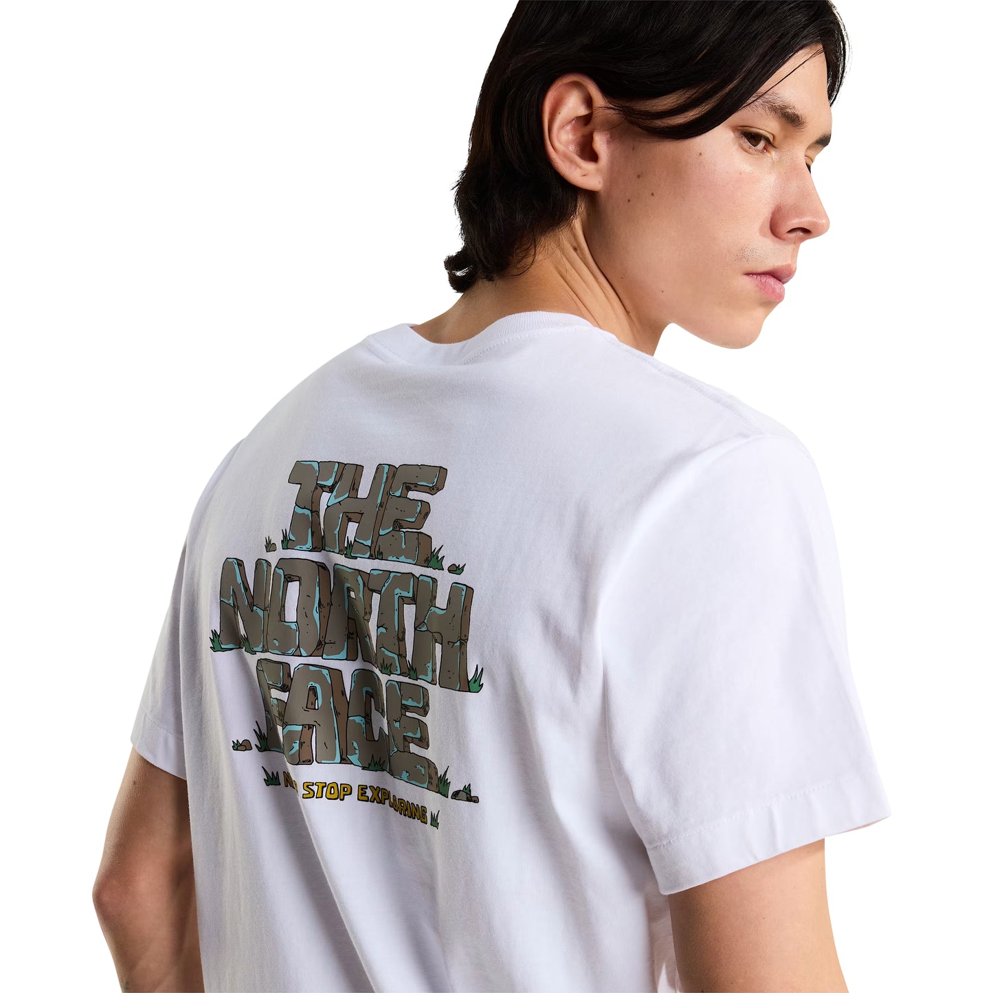 T-Shirt The North Face Stone Logo Relaxed em TNF White — detalhe das costas de modelo masculino, gráfico "The North Face" estilo pedra em cinza/verde musgo com detalhes de erva e inscrição "Never Stop Exploring" em amarelo na base visíveis em close-up, fundo branco.