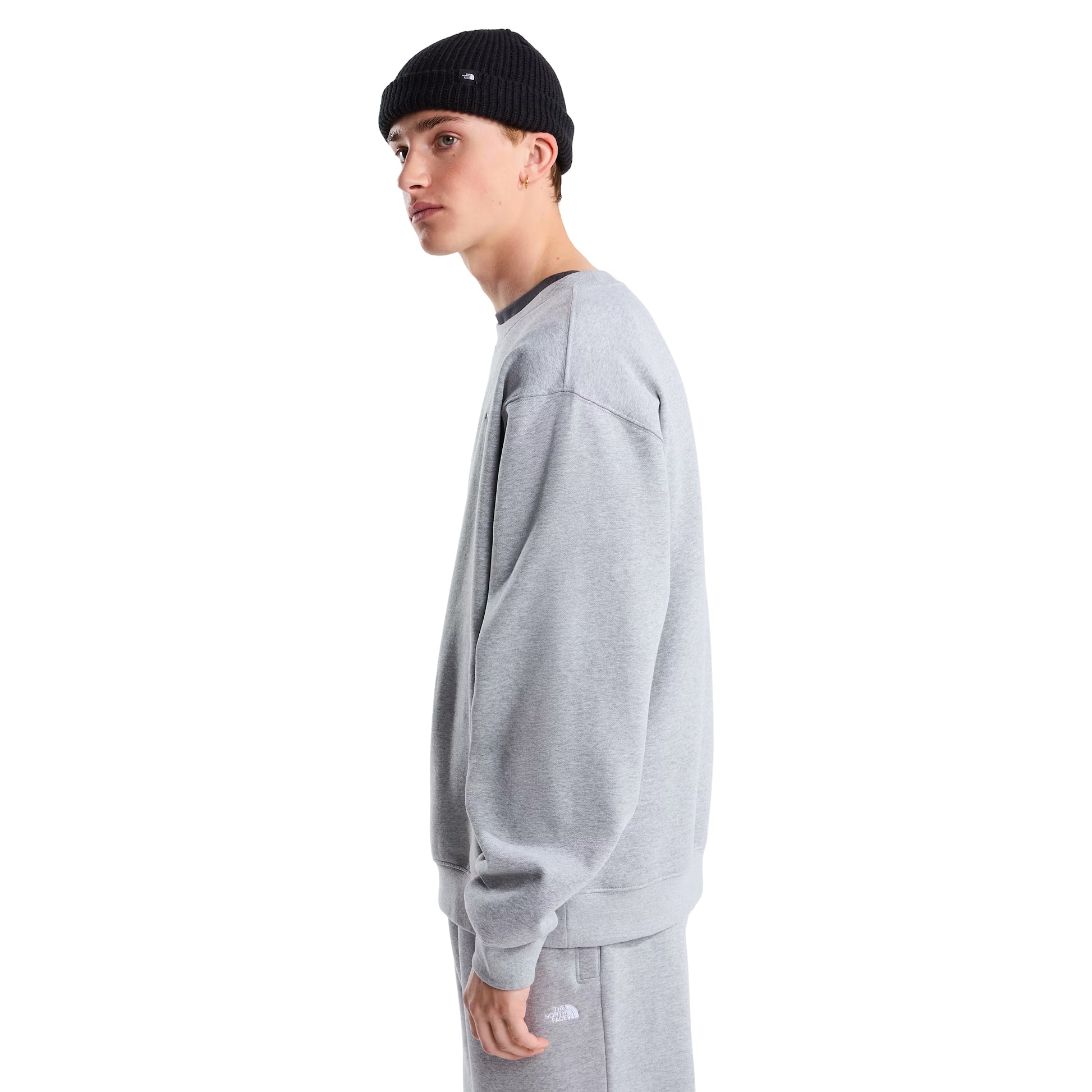 Sweat The North Face TNF Essential Simple Dome Relaxed em TNF Pale Grey Heather — modelo masculino de perfil direito, corpo inteiro, gorro preto TNF, calças de fato de treino TNF Pale Grey Heather, corte relaxado com costuras dos ombros e punhos canelados visíveis, fundo branco.