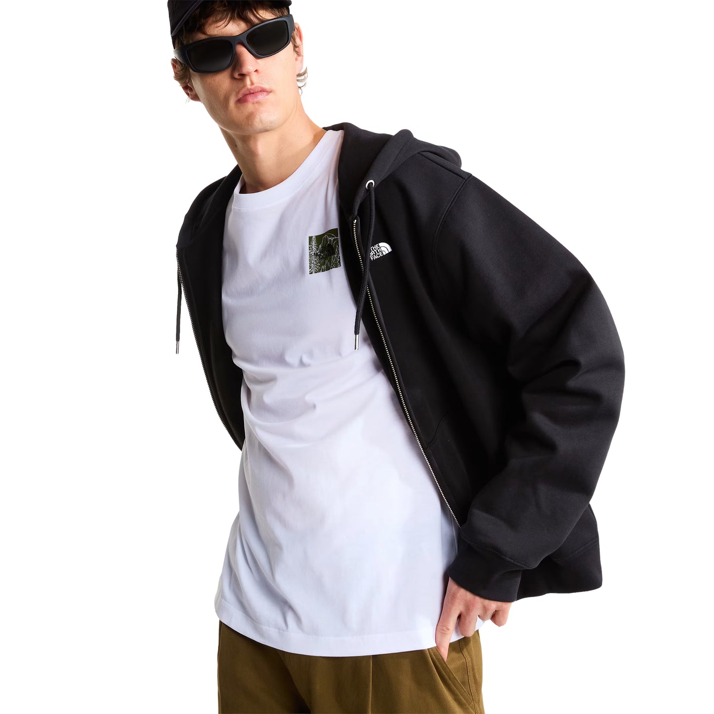 Hoodie The North Face TNF Essential Simple Dome Relaxed Full Zip em TNF Black — modelo masculino de frente a 3/4, boné preto, óculos de sol escuros, hoodie aberta sobre t-shirt branca com patch TNF no peito, logótipo TNF half-dome bordado em branco e fecho de correr integral prateado visíveis, fundo branco.
