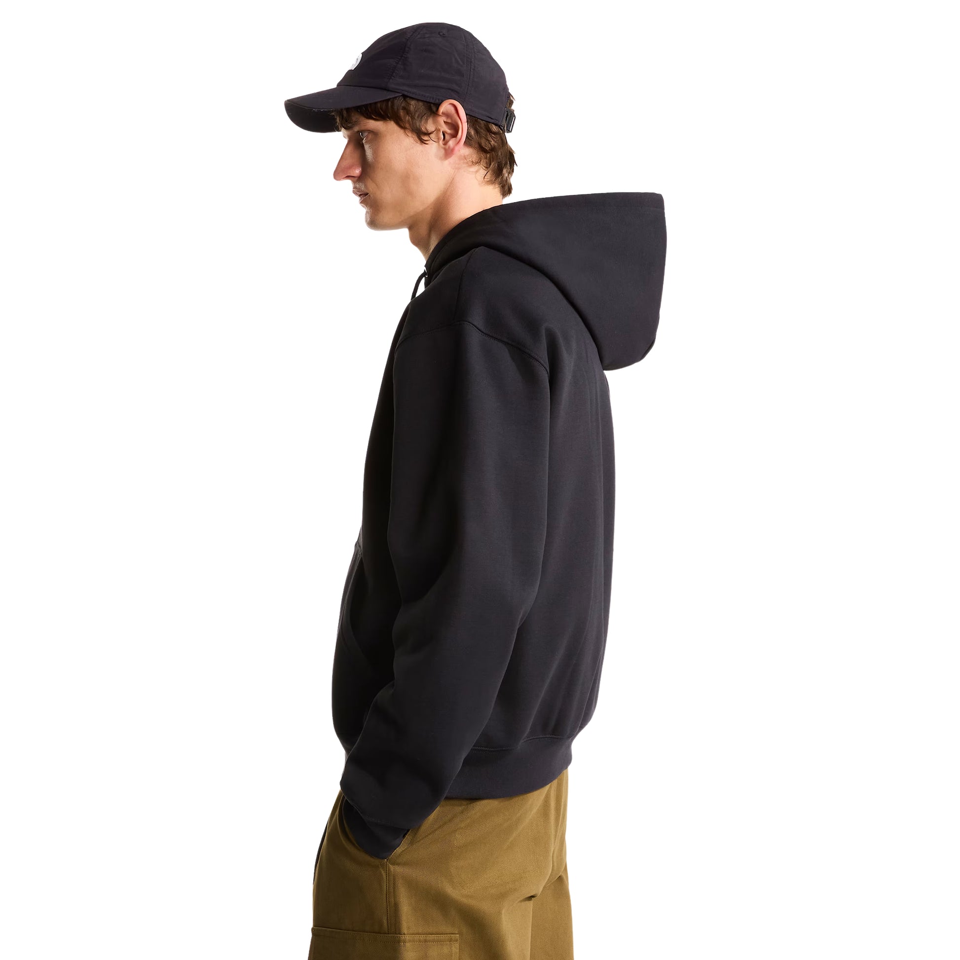 Hoodie The North Face TNF Essential Simple Dome Relaxed Full Zip em TNF Black — modelo masculino de perfil esquerdo, boné TNF preto, calças cargo verde-oliva, capuz com pregas e cordão branco, corte relaxado com manga larga e punho canelado visíveis, fundo branco.