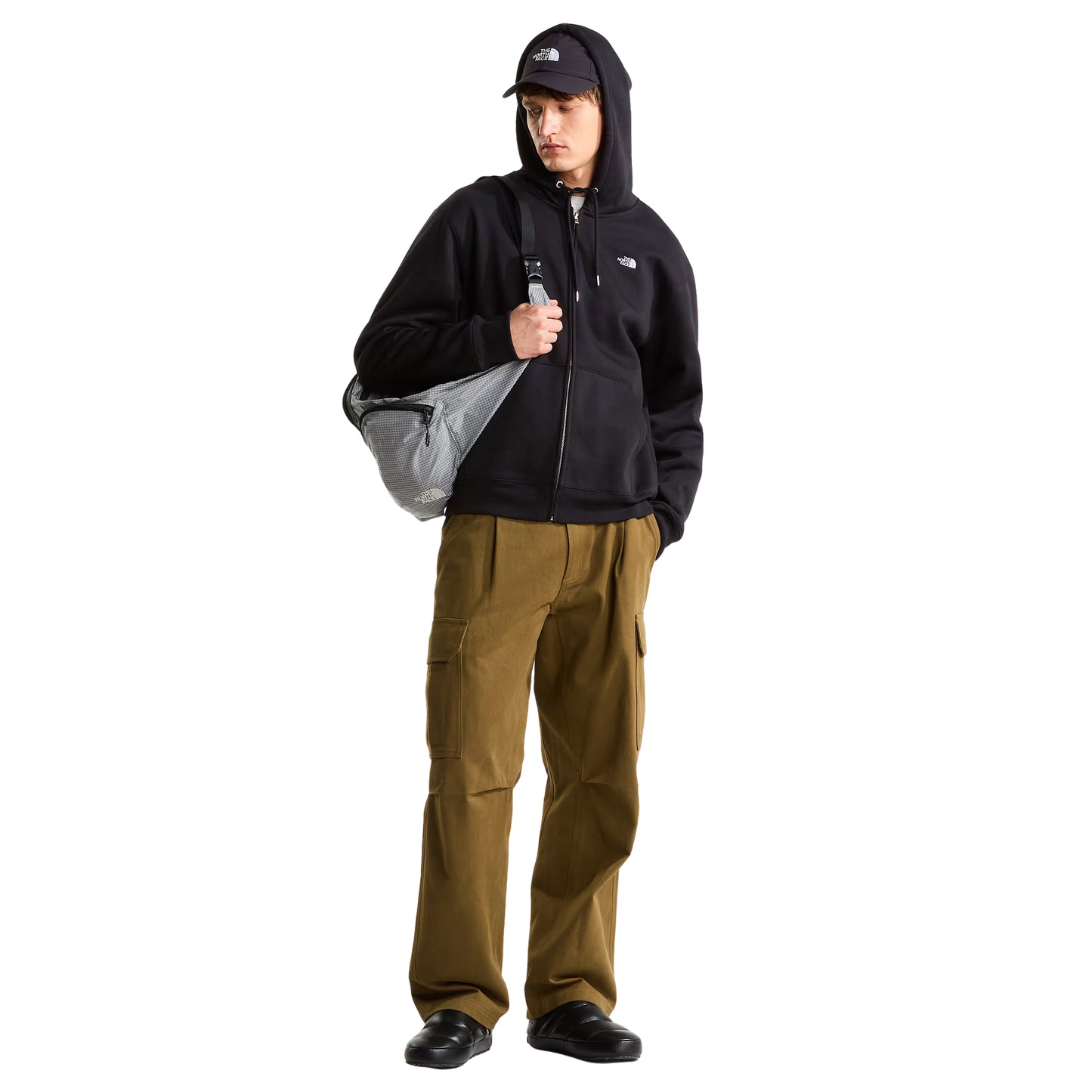 Hoodie The North Face TNF Essential Simple Dome Relaxed Full Zip em TNF Black — modelo masculino de frente, corpo inteiro, boné TNF preto, calças cargo verde-oliva largas, sapatilhas pretas, mochila TNF cinza ao ombro, hoodie fechada com logótipo TNF half-dome bordado em branco e bolso canguru visíveis, fundo branco.