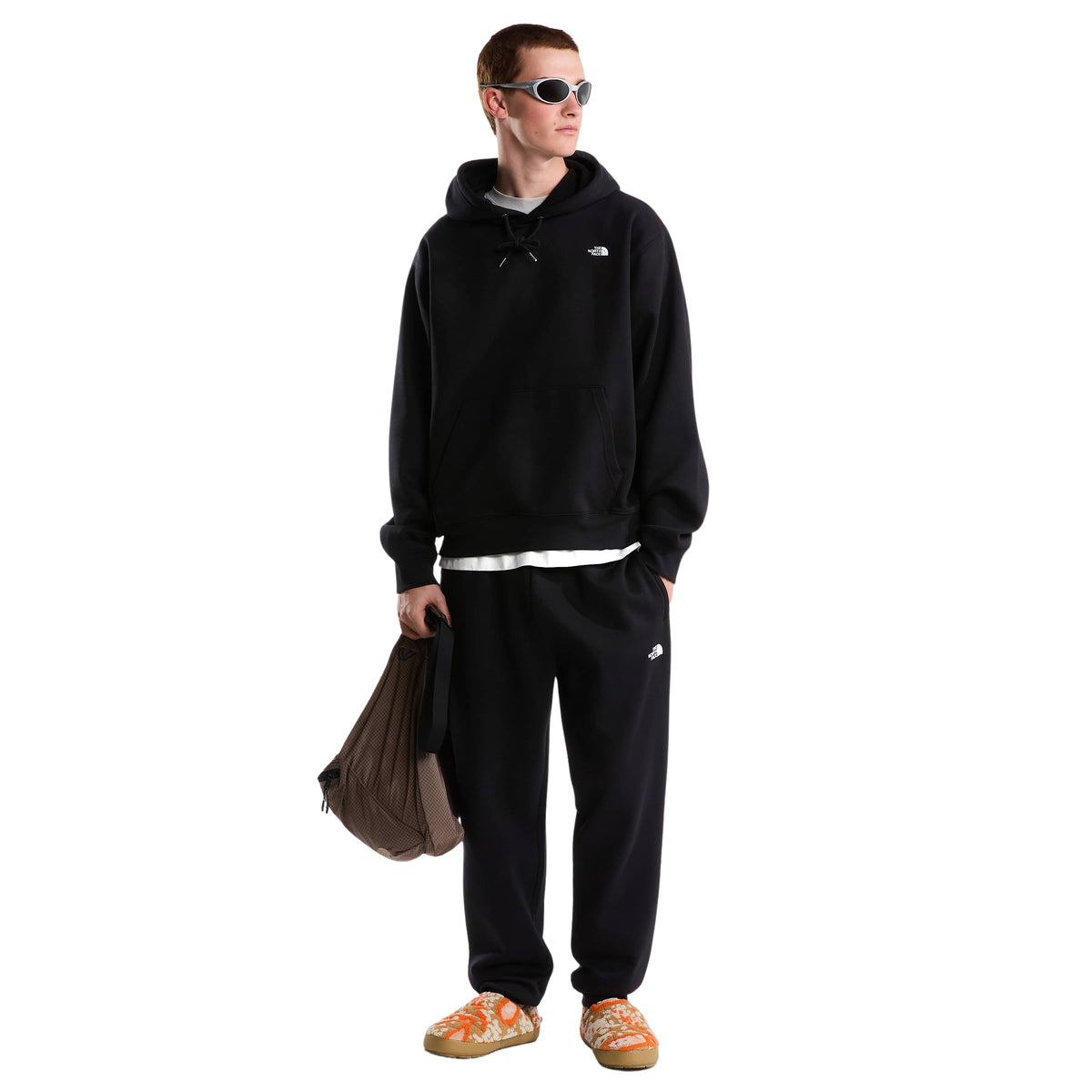 Modelo de corpo inteiro com sweat The North Face Essential Simple Dome preta, calças pretas, óculos de sol e mochila na mão.