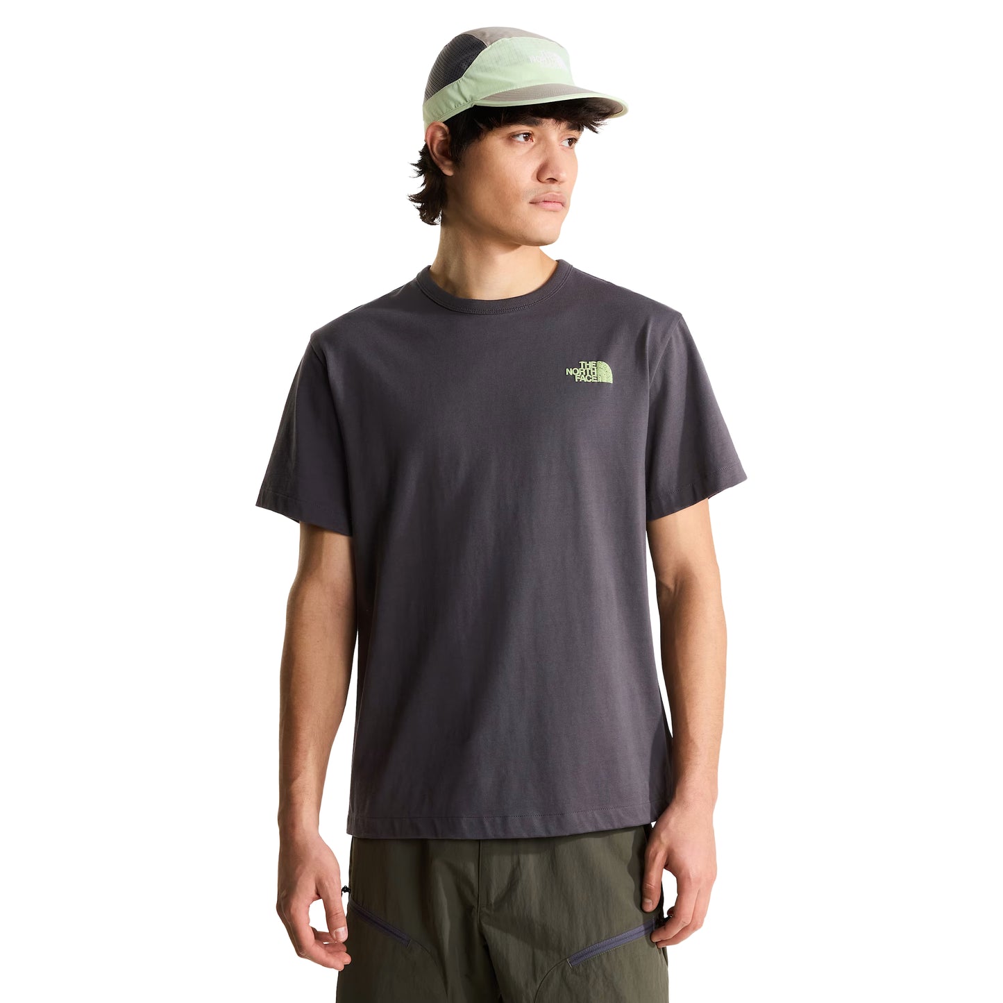 T-shirt unissexo The North Face NSE Slopes Relaxed em Anthracite Grey — modelo masculino de frente, meio corpo, boné técnico branco e cinza TNF, logótipo "The North Face" half-dome estampado em relevo verde lima no peito esquerdo, gola canelada e jersey Anthracite Grey visíveis, fundo branco.