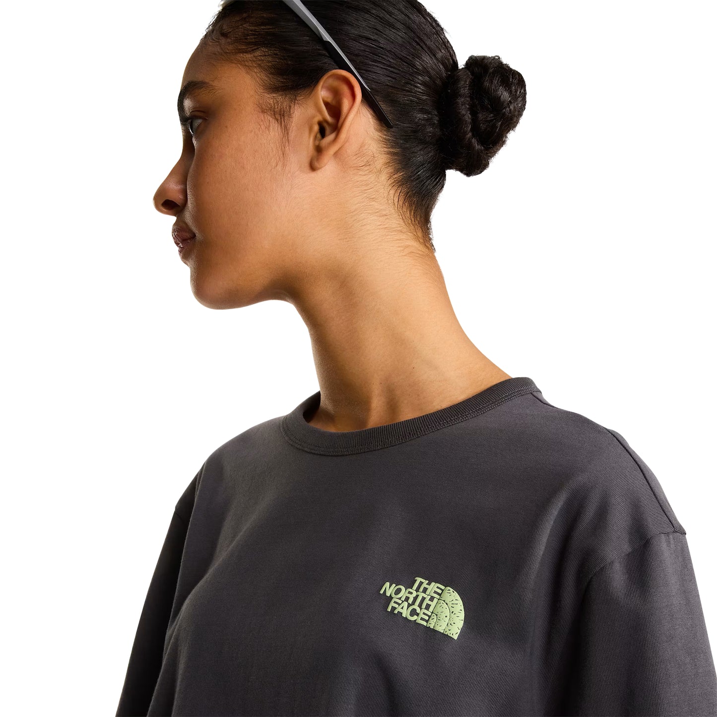 T-shirt unissexo The North Face NSE Slopes Relaxed em Anthracite Grey — modelo feminino de frente, meio corpo, óculos de sol brancos na cabeça, calças cargo verde-oliva, logótipo "The North Face" half-dome estampado em relevo verde lima no peito esquerdo, gola canelada e jersey Anthracite Grey visíveis, fundo branco.