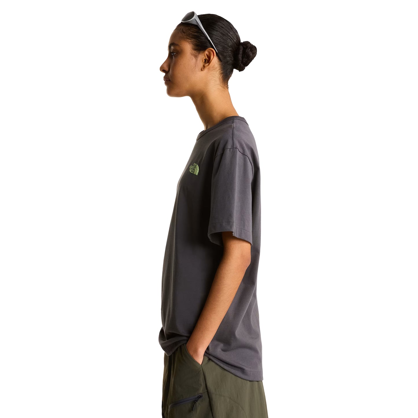 T-shirt unissexo The North Face NSE Slopes Relaxed em Anthracite Grey — modelo feminino de perfil esquerdo, corpo inteiro, óculos de sol brancos na cabeça, calças cargo verde-oliva, logótipo "The North Face" half-dome estampado em verde lima no peito esquerdo, corte relaxado com comprimento alongado visível, fundo branco.