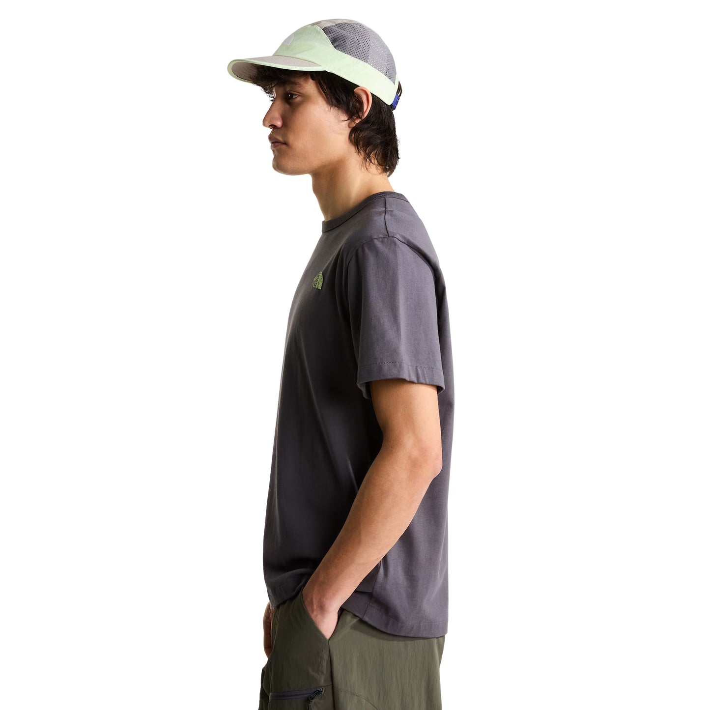 T-shirt unissexo The North Face NSE Slopes Relaxed em Anthracite Grey — modelo masculino de perfil esquerdo, corpo inteiro, boné técnico branco e cinza TNF, calças cargo verde-oliva, corte relaxado com ombros descaídos e jersey Anthracite Grey visíveis, fundo branco.
