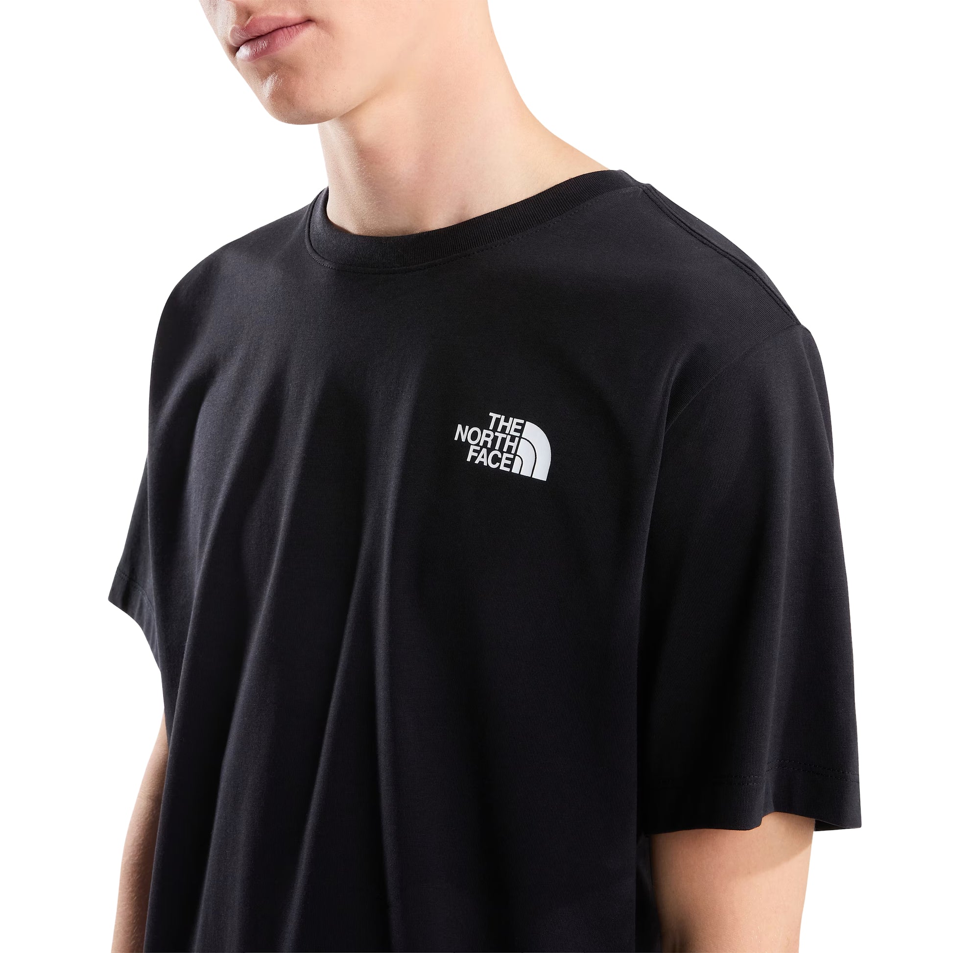 T-Shirt The North Face Vertical Regular em TNF Black — detalhe do peito de modelo masculino, logo TNF half-dome em branco no peito esquerdo e gola redonda visíveis em close-up, fundo branco.