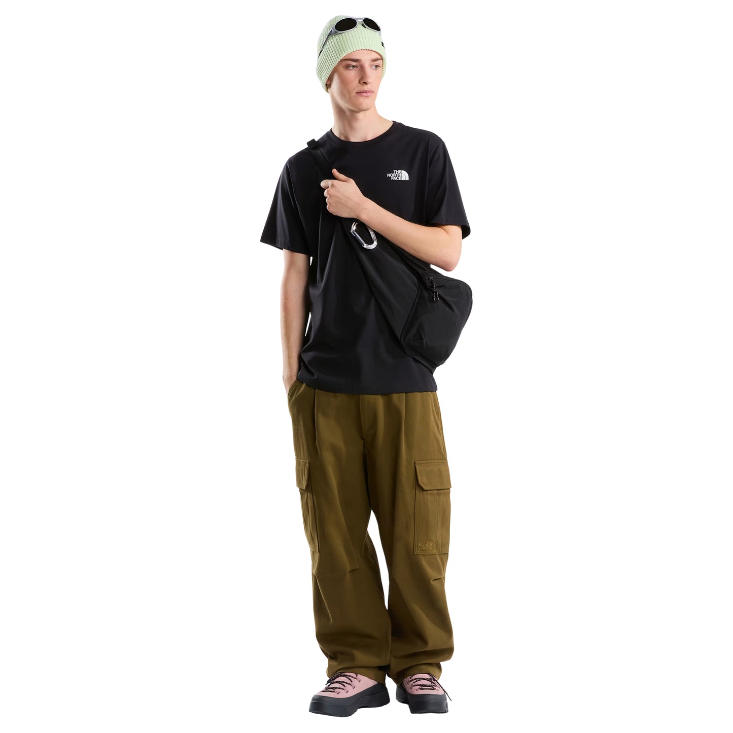T-Shirt The North Face Vertical Regular em TNF Black — modelo masculino de costas, corpo inteiro, gorro TNF verde-lima, calças cargo bege/cáqui largas e sapatilhas brancas, gráfico vertical "The North Face" em branco nas costas visível, fundo branco.