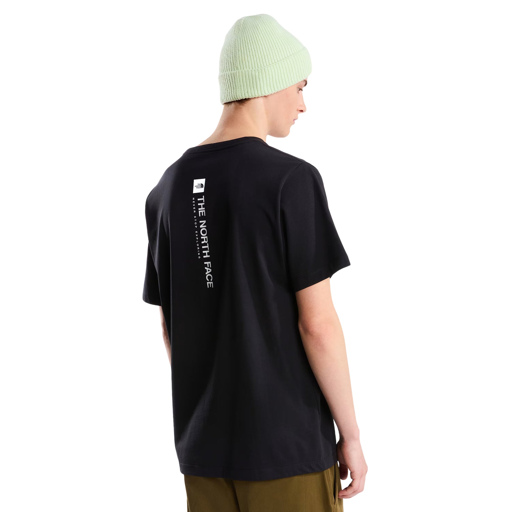 T-Shirt The North Face Vertical Regular em TNF Black — modelo masculino de perfil esquerdo, gorro TNF verde-lima, calças cargo bege/cáqui largas, gola redonda e manga curta com corte regular visíveis, fundo branco.