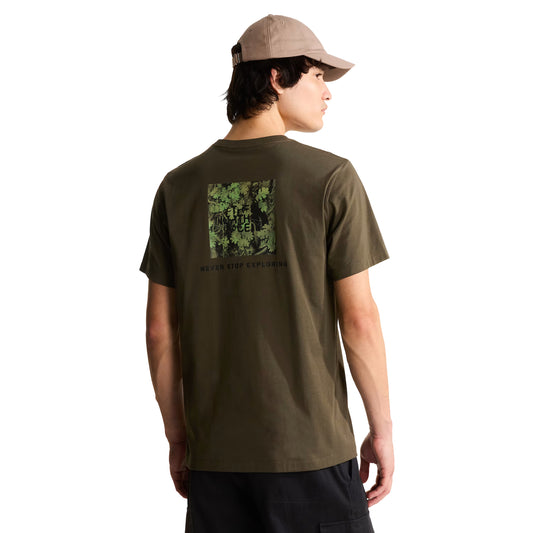 T-Shirt The North Face Yosemite Oak Box NSE Regular em New Taupe Green — modelo masculino de costas a 3/4, boné TNF bege/taupe, calças cargo pretas, gráfico em caixa com folhas de carvalho Yosemite em verde-floresta e logo TNF com inscrição "Never Stop Exploring" em preto nas costas visíveis, fundo branco.