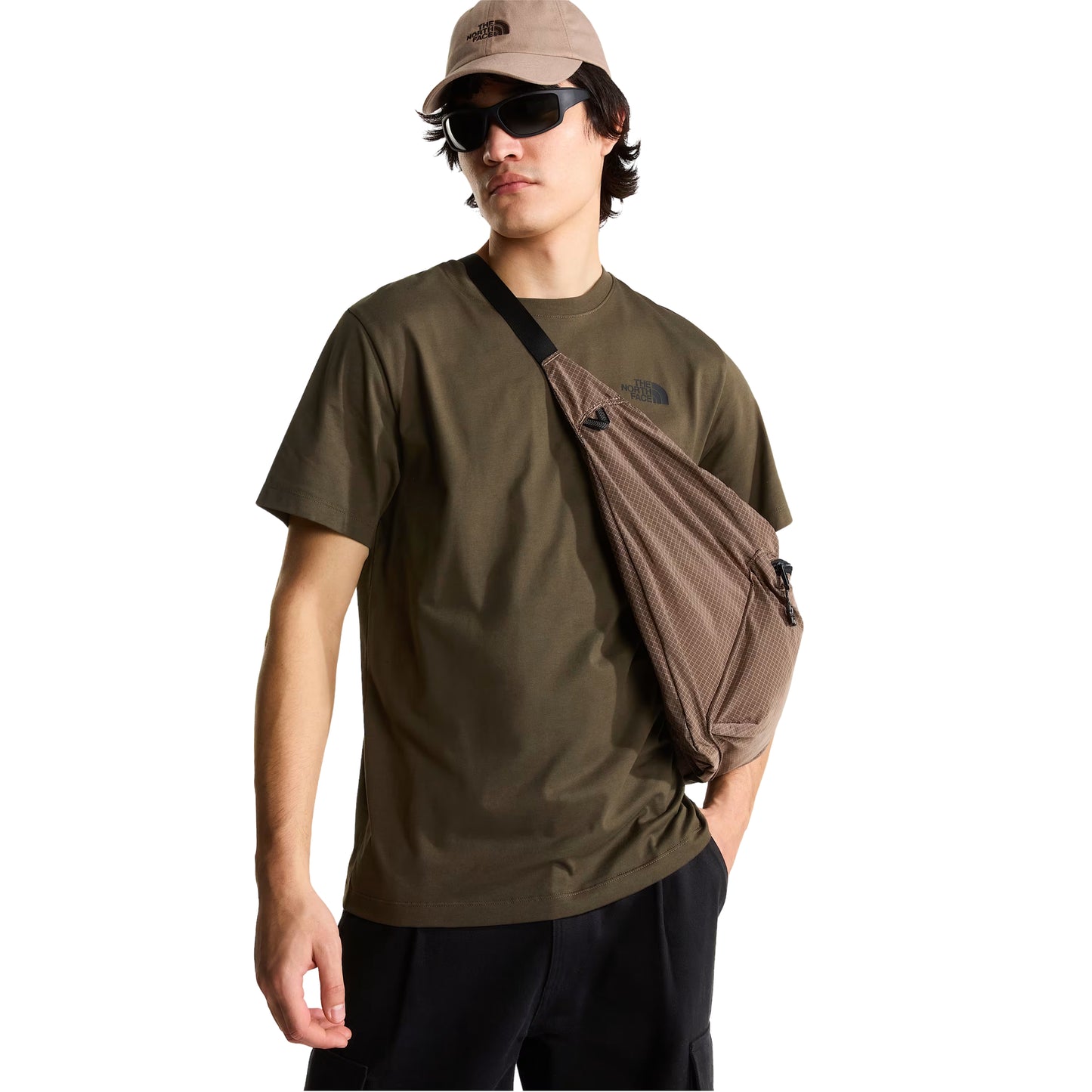 T-Shirt The North Face Yosemite Oak Box NSE Regular em New Taupe Green — modelo masculino de frente a 3/4, boné TNF bege/taupe, óculos de sol escuros, mochila sling TNF bege/taupe em tiracolo, calças cargo pretas, logo TNF no peito esquerdo visível, fundo branco.