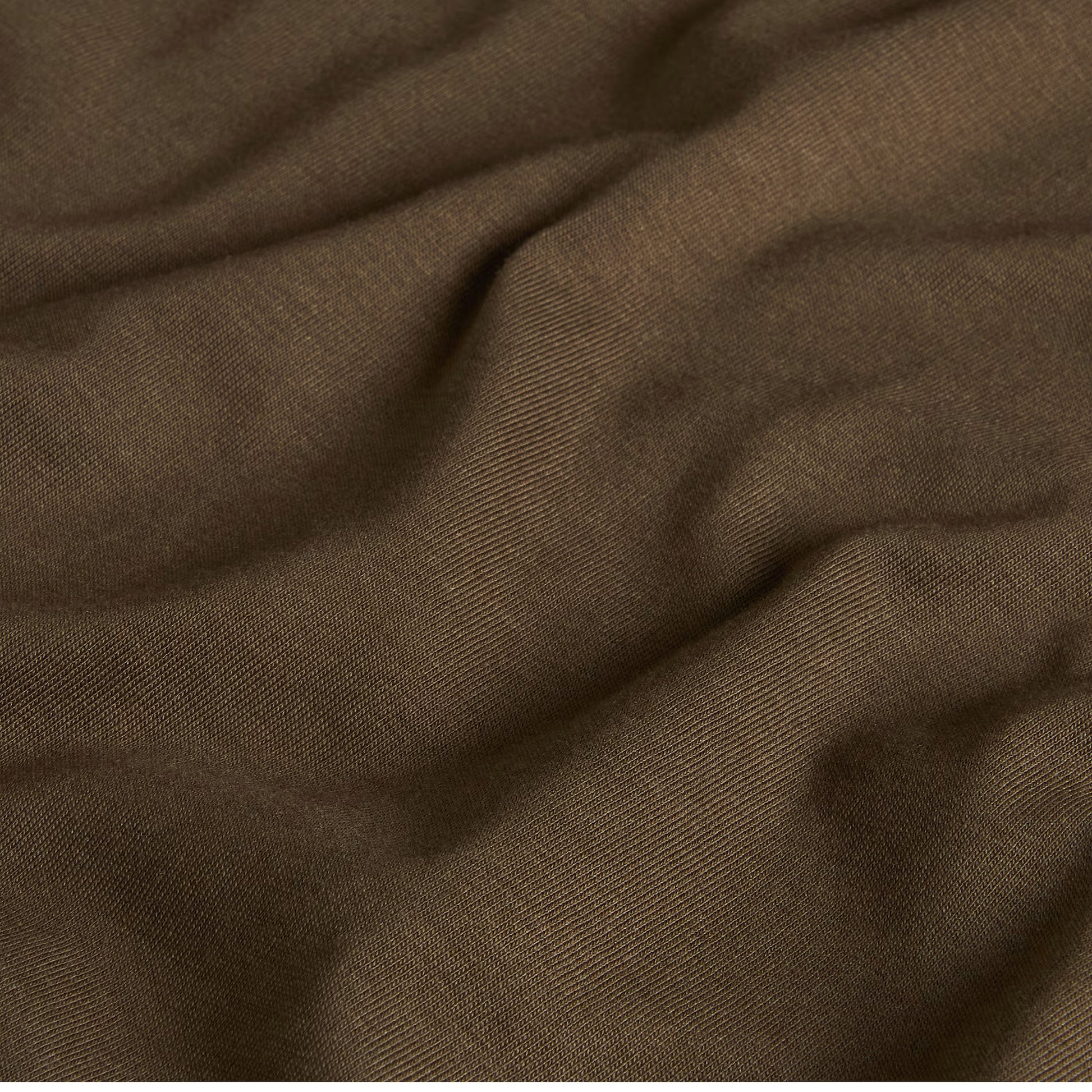 T-Shirt The North Face Yosemite Oak Box NSE Regular em New Taupe Green — detalhe do tecido jersey em New Taupe Green, textura de malha 165 g/m² com dobras suaves visíveis em close-up, fundo escuro.