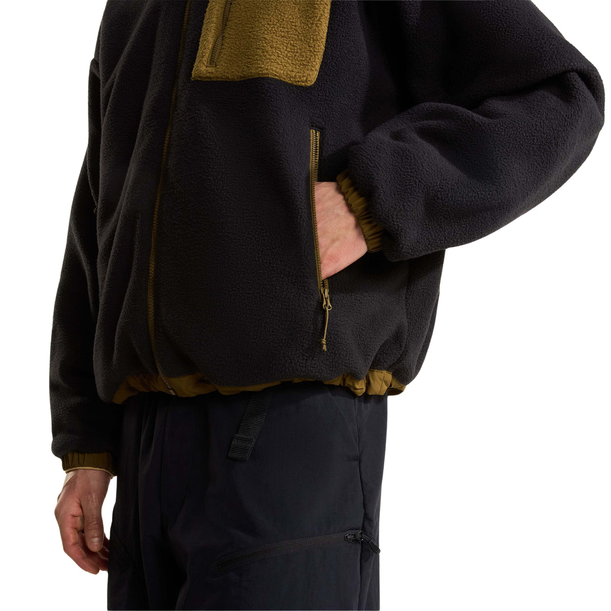 Pormenor do bolso lateral com fecho do casaco polar The North Face Yumiori preto, com a mão no interior.