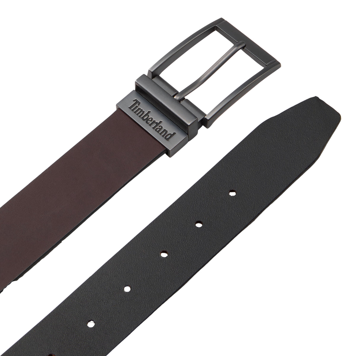 Cinto reversível Timberland Bartley para homem em Castanho/Preto — detalhe das duas faces da correia: castanho liso na frente e preto liso no verso, fivela reversível em cinza fosco com logo Timberland gravado e furos visíveis na face preta, fundo branco.