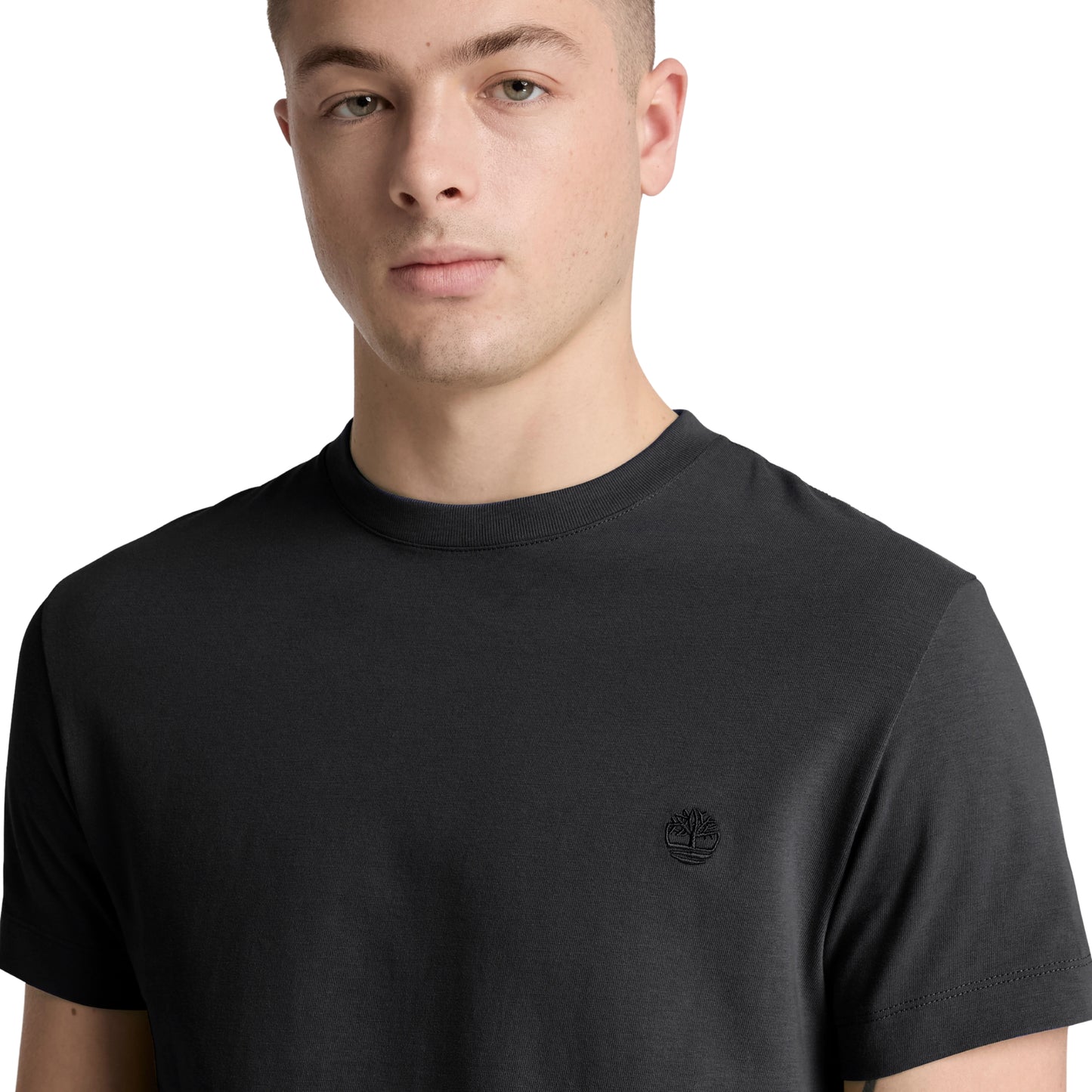 T-shirt Timberland Dunstan River em Black — detalhe do logótipo árvore Timberland bordado em preto tonal no peito esquerdo e gola redonda canelada, close-up com modelo.