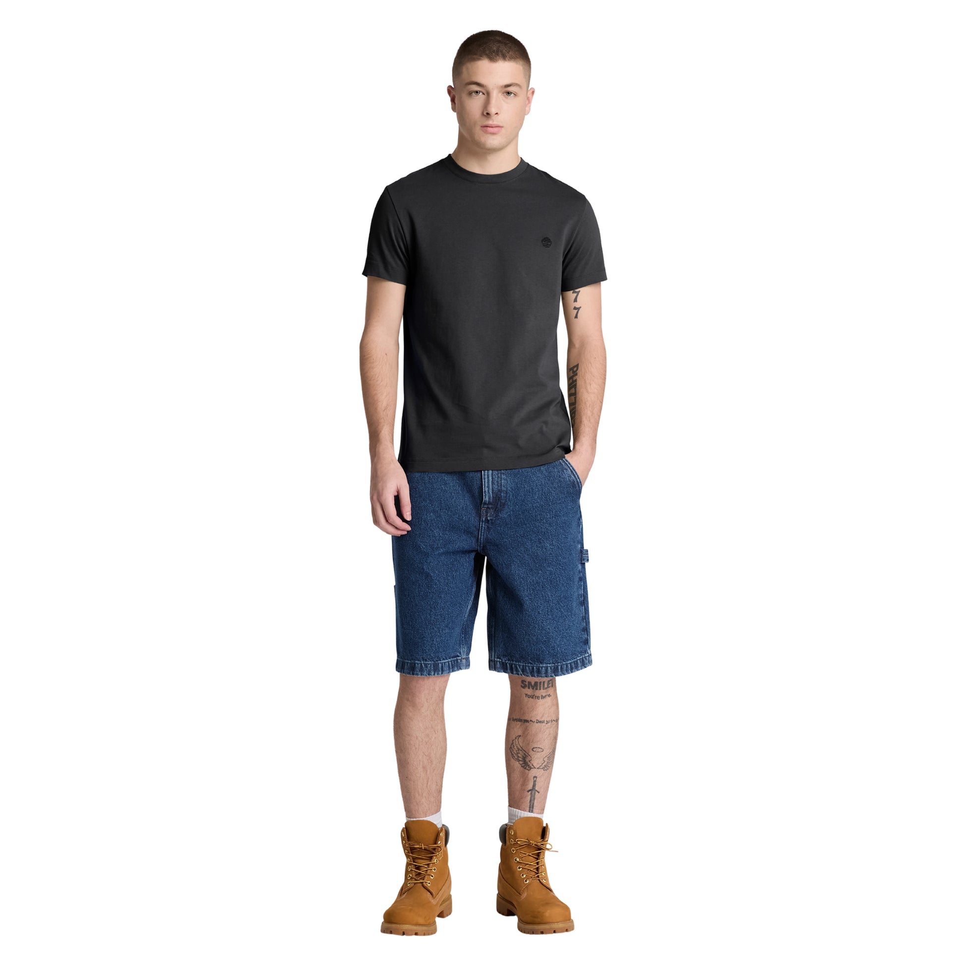 T-shirt Timberland Dunstan River em Black — vista frontal com modelo, corpo inteiro, corte slim e comprimento ligeiramente curto visíveis, combinado com calções denim azul e botas wheat Timberland.