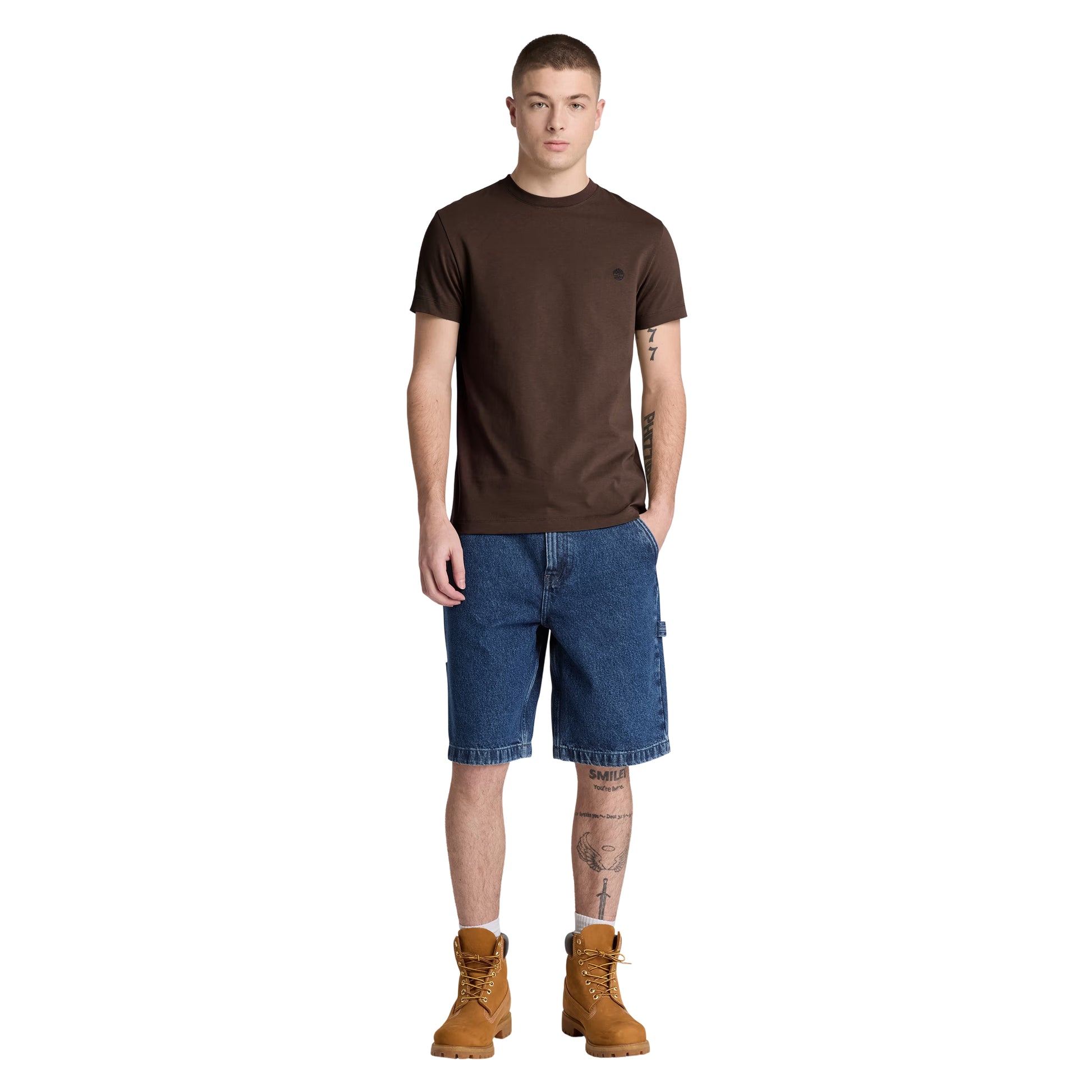 T-shirt Timberland Dunstan River em Mole — vista frontal com modelo, corpo inteiro, corte slim e comprimento ligeiramente curto visíveis, combinado com calções denim azul e botas wheat Timberland.