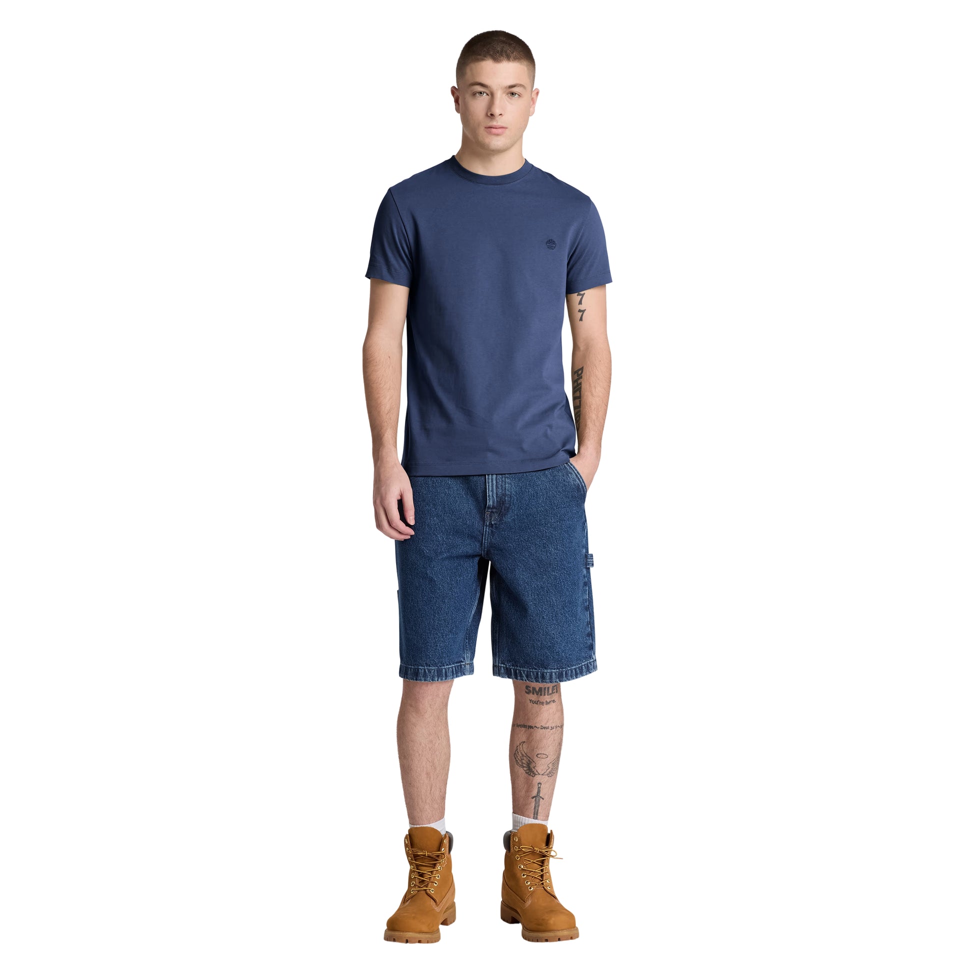 T-shirt Timberland Dunstan River em Naval Academy — vista frontal com modelo, corpo inteiro, corte slim e comprimento ligeiramente curto visíveis, combinado com calções denim azul e botas wheat Timberland.