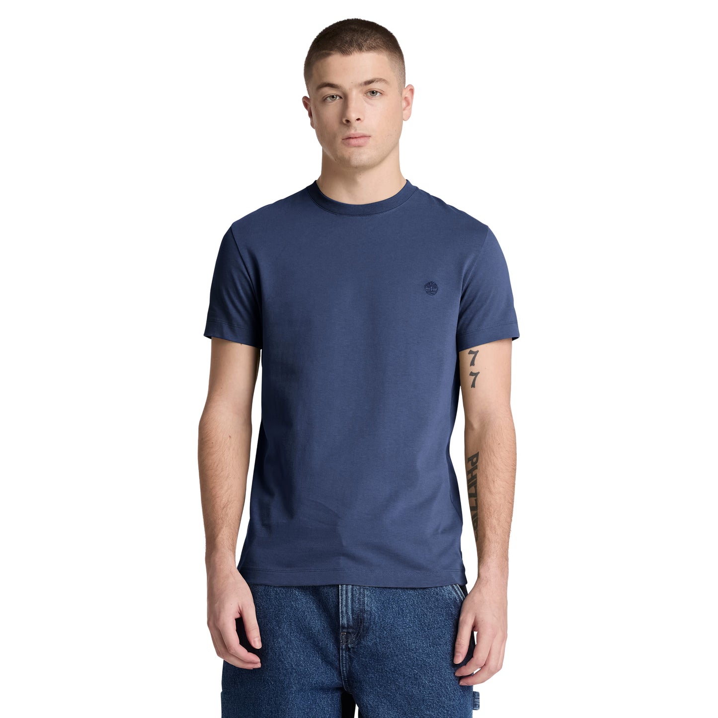 T-shirt Timberland Dunstan River em Naval Academy — vista frontal com modelo, meio corpo, logótipo árvore Timberland bordado em preto tonal no peito esquerdo, gola redonda canelada, corte slim, combinado com calções denim azul.