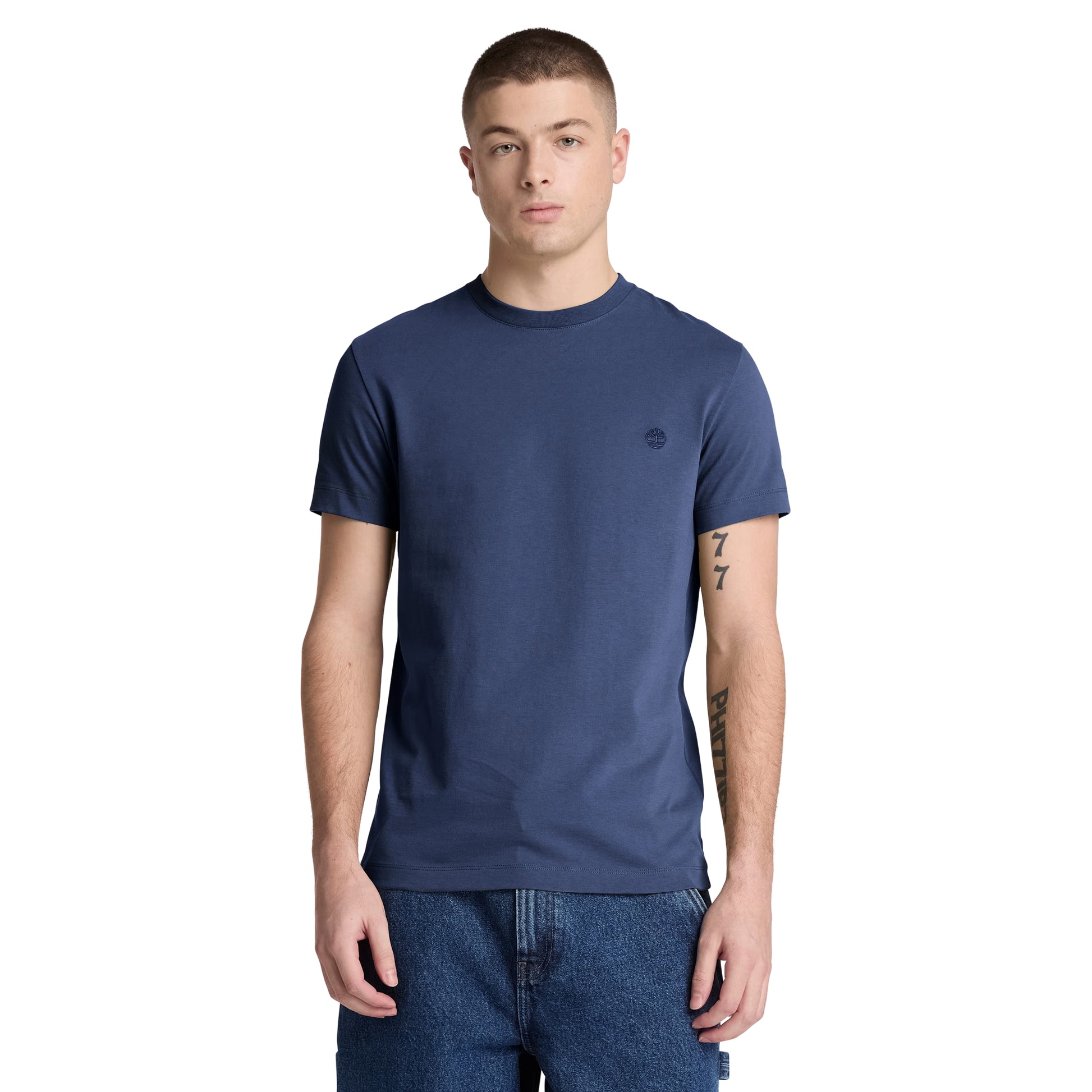 T-shirt Timberland Dunstan River em Naval Academy — vista frontal com modelo, meio corpo, logótipo árvore Timberland bordado em preto tonal no peito esquerdo, gola redonda canelada, corte slim, combinado com calções denim azul.