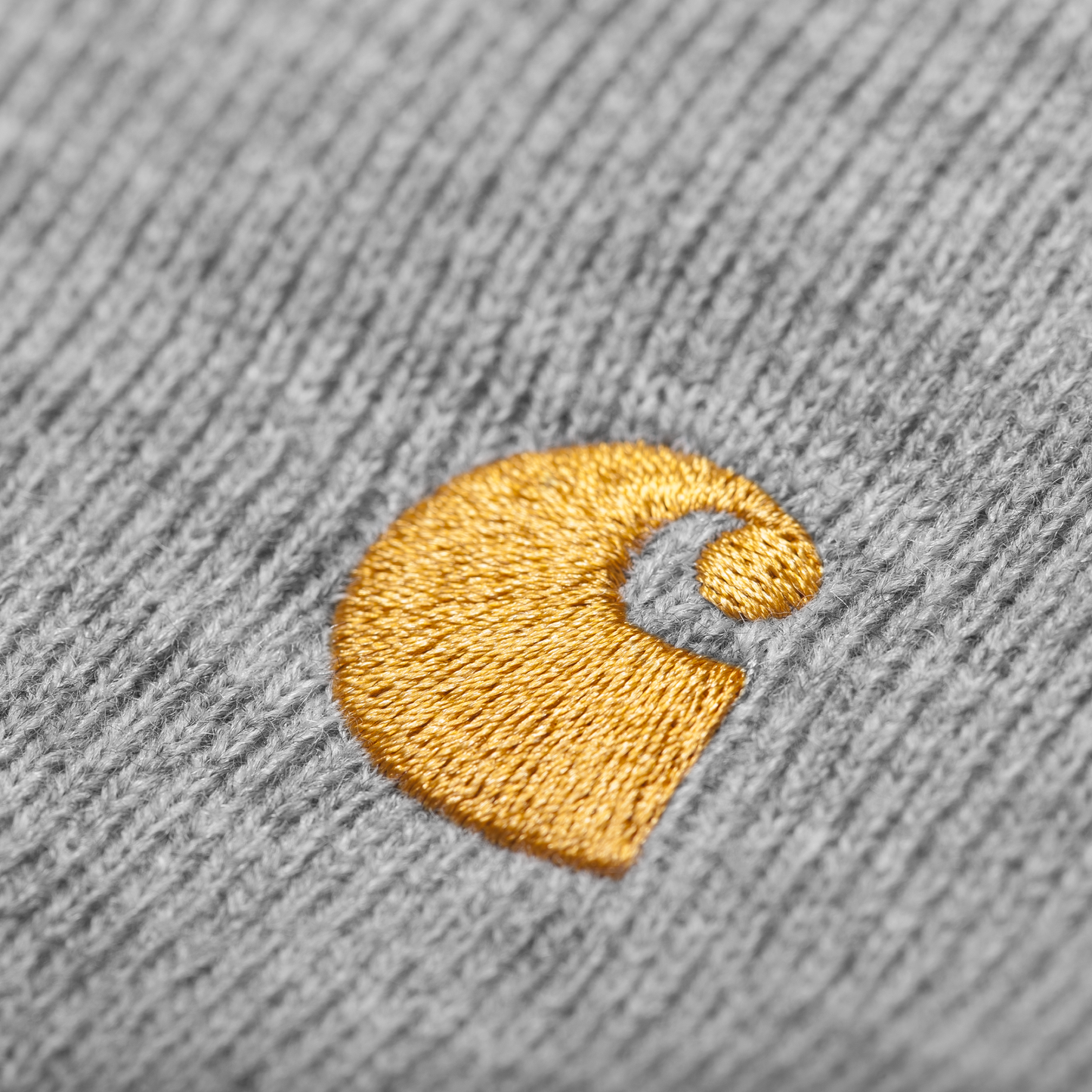 Carhartt WIP Chase Beanie em Grey Heather com logo bordado na frente em dourado. Foto de detalhe do logo bordado na frente.