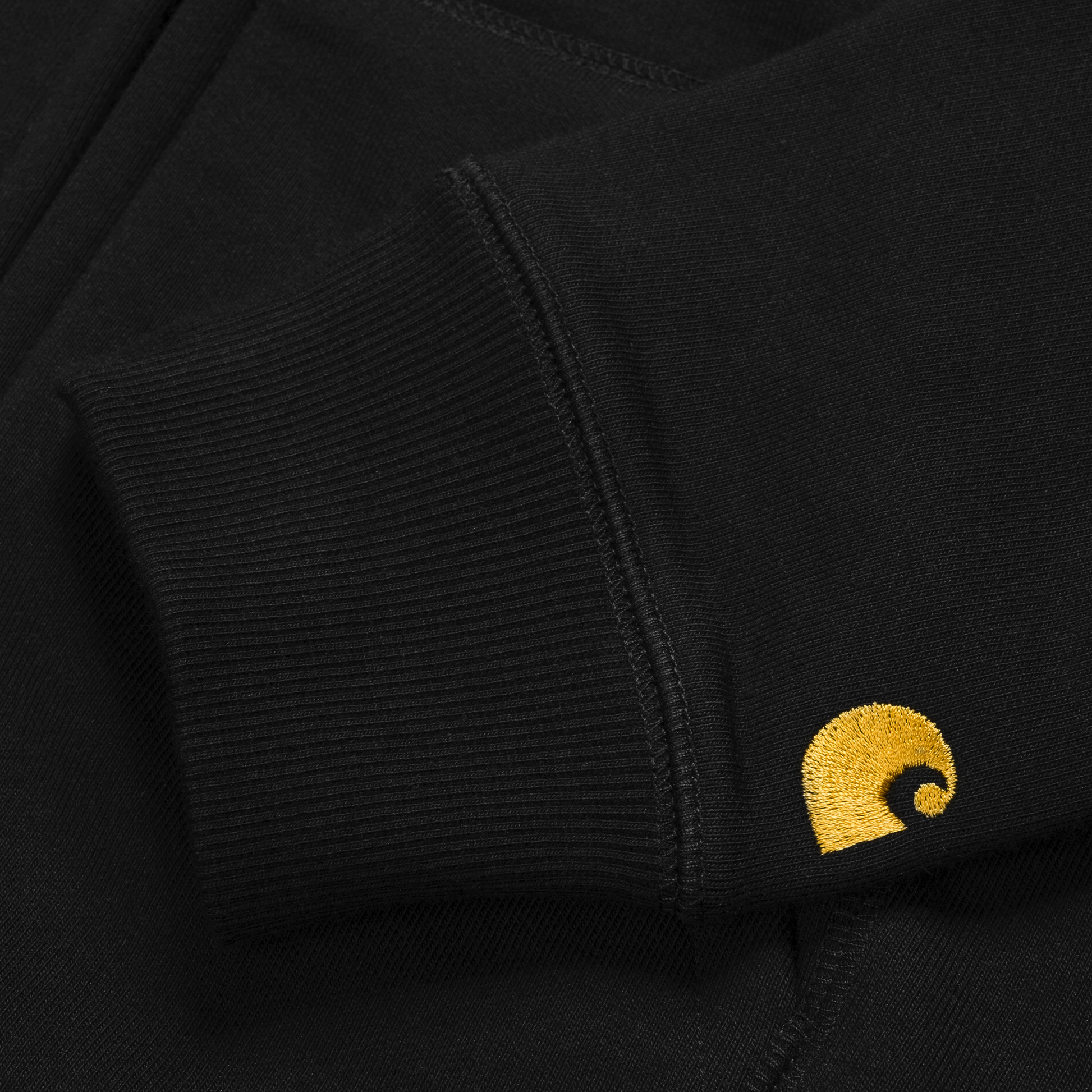 Carhartt WIP Hooded Chase Jacket em preto com logo bordado na manga em dourado. Foto de detalhe do logo bordado na manga.