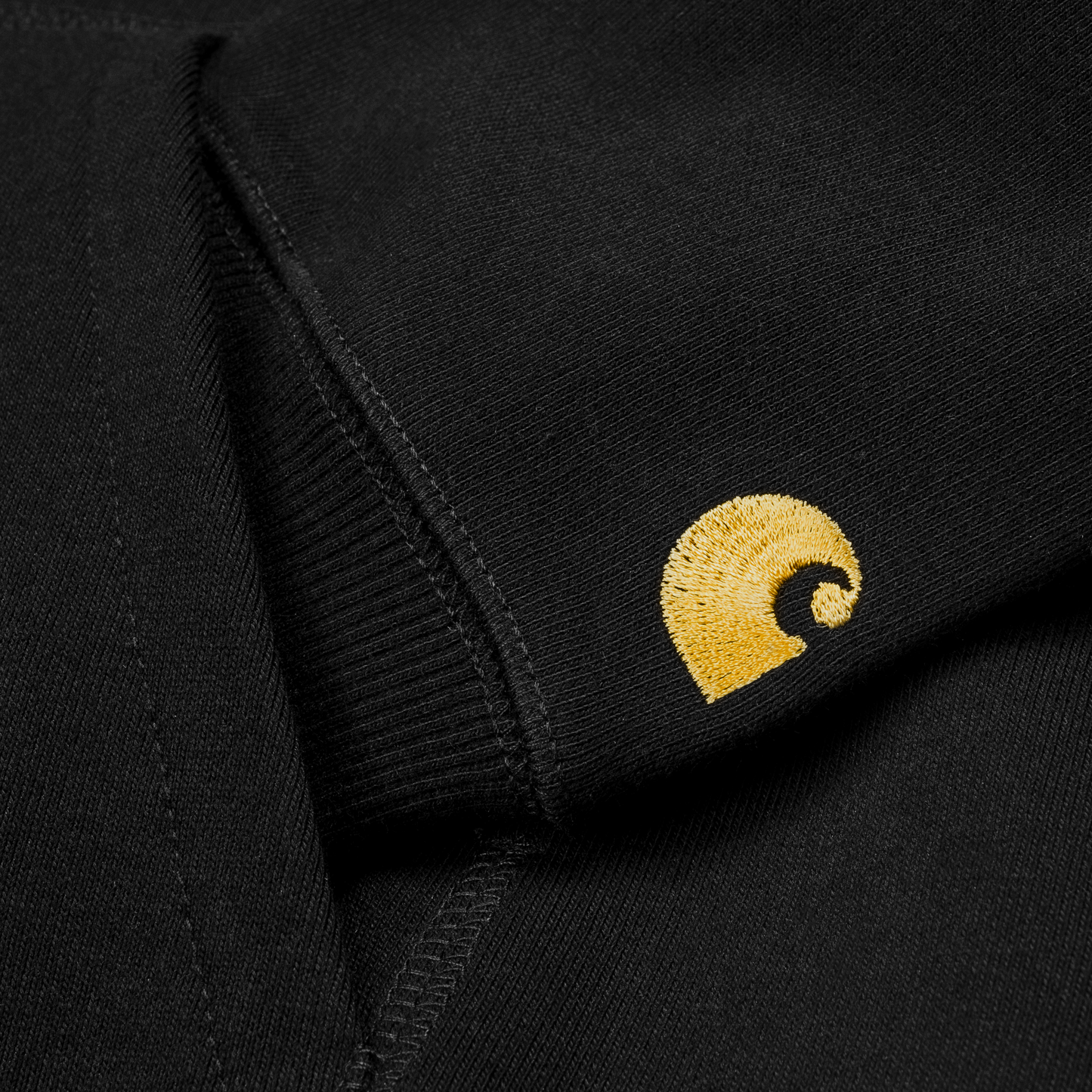 Carhartt WIP Hooded Chase Sweat em preto com detalhes em dourado. Foto de detalhe do bordado na manga.