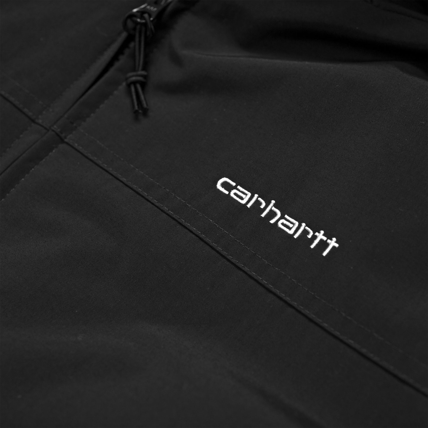 Carhartt WIP Hooded Sail Jacket em preto com logo bordado na frente em branco. Foto de detalhe do logo bordado.